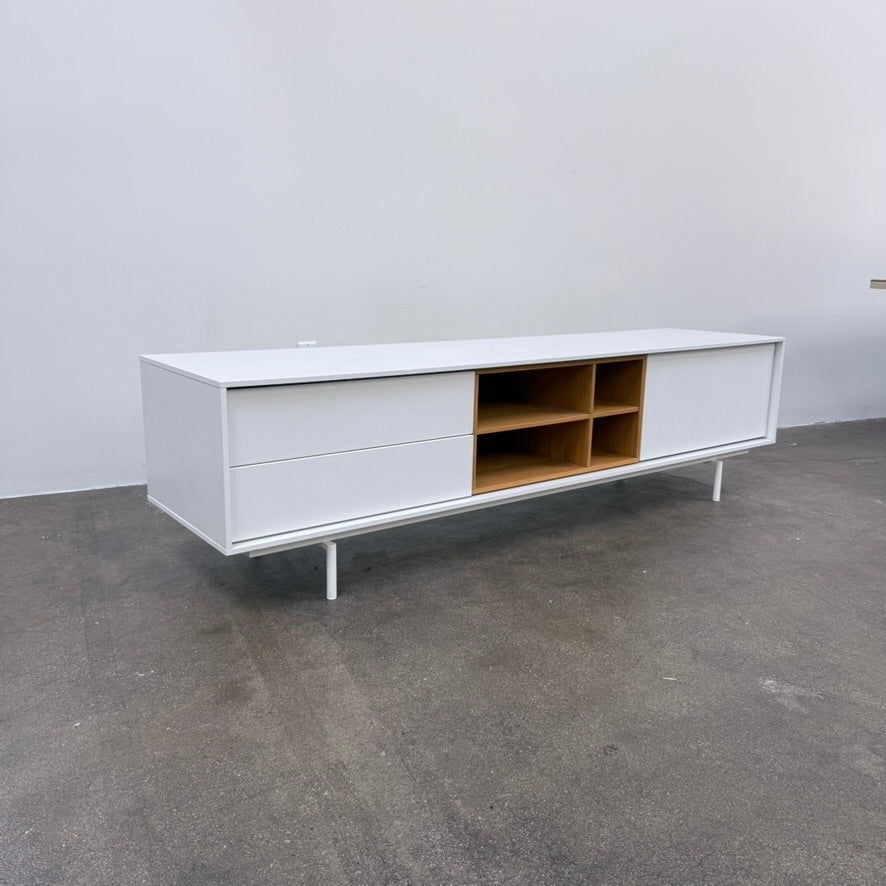 Low-profile white DWR Treku Aura Media Unit on thin legs, featuring two side cabinets and a central open shelf section with a wood-toned interior.