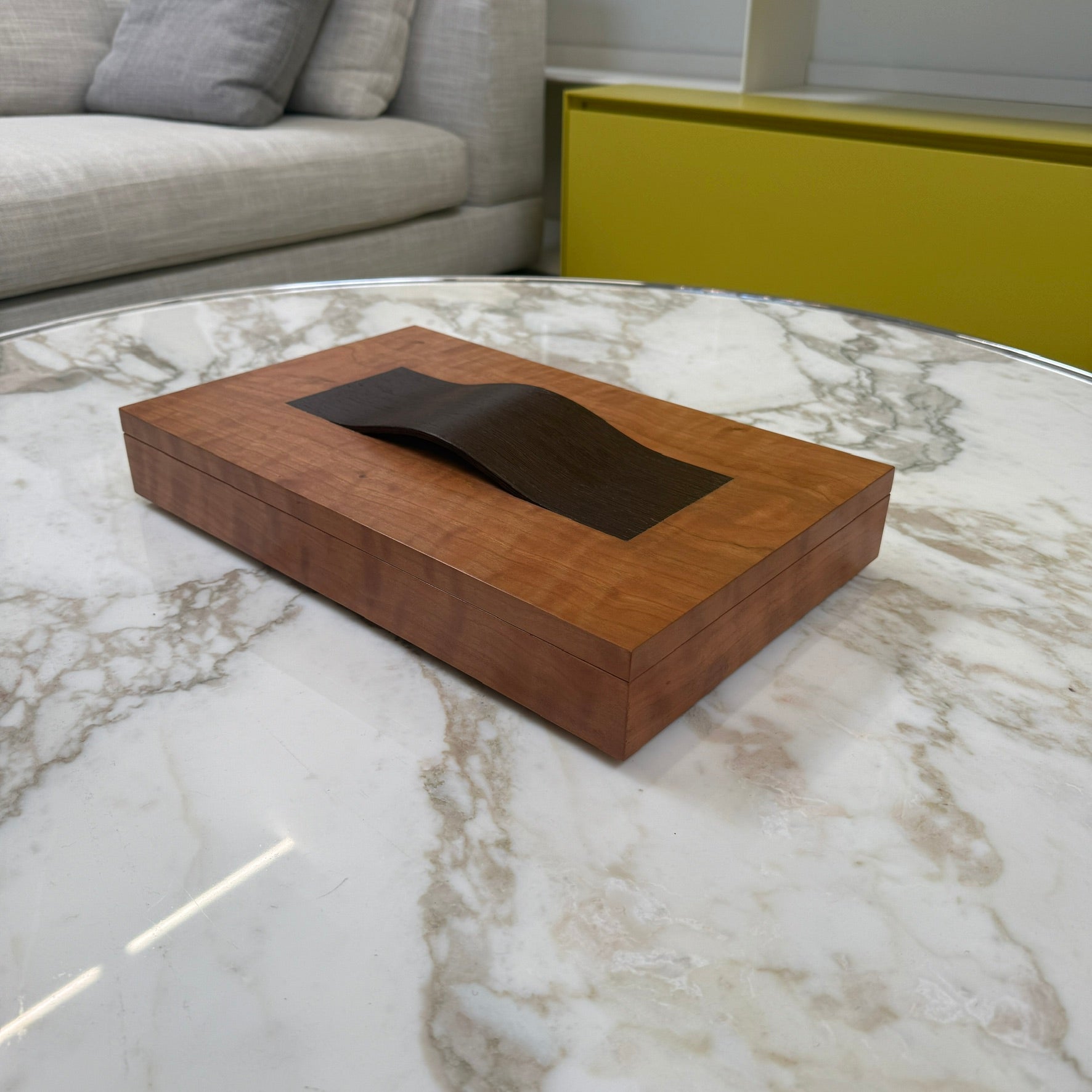 The Mike Fair Jewelry Box / Cigar Box by Mike Fair Custom Furnishings is a rectangular cherry wood box with a smooth finish and a curved, dark handle on the lid, displayed against a plain white background.