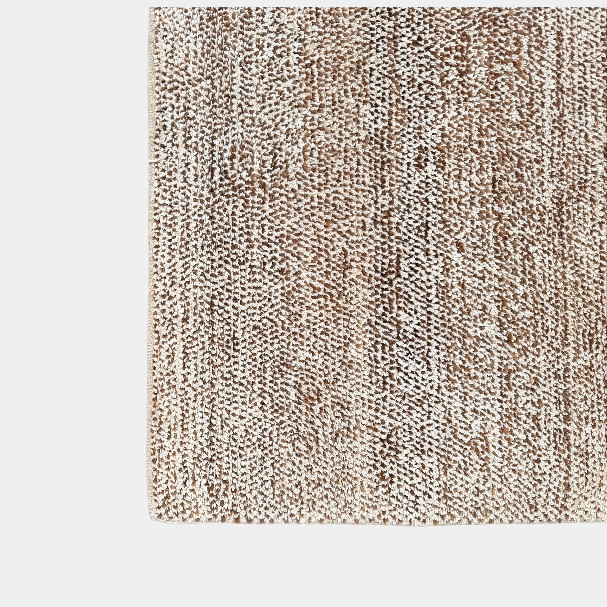Close-up of the textured beige and brown woven surface of the ABC Carpet and Home 8'x10' rug by Modern Resale, featuring a subtle pattern. A small fabric tag can be seen in the upper left corner.