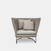 The Paola Lenti Ami Outdoor Armchair by Paola Lenti features a large weave frame, light gray cushions, and a metal base, all set against a plain white background.