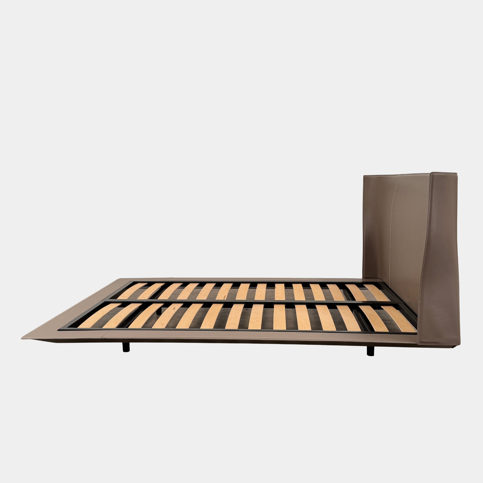 The B&B Italia Alys Queen Size Bed in Tortora Leather features a tall upholstered headboard and wooden slats, shown from a side angle against a plain background.