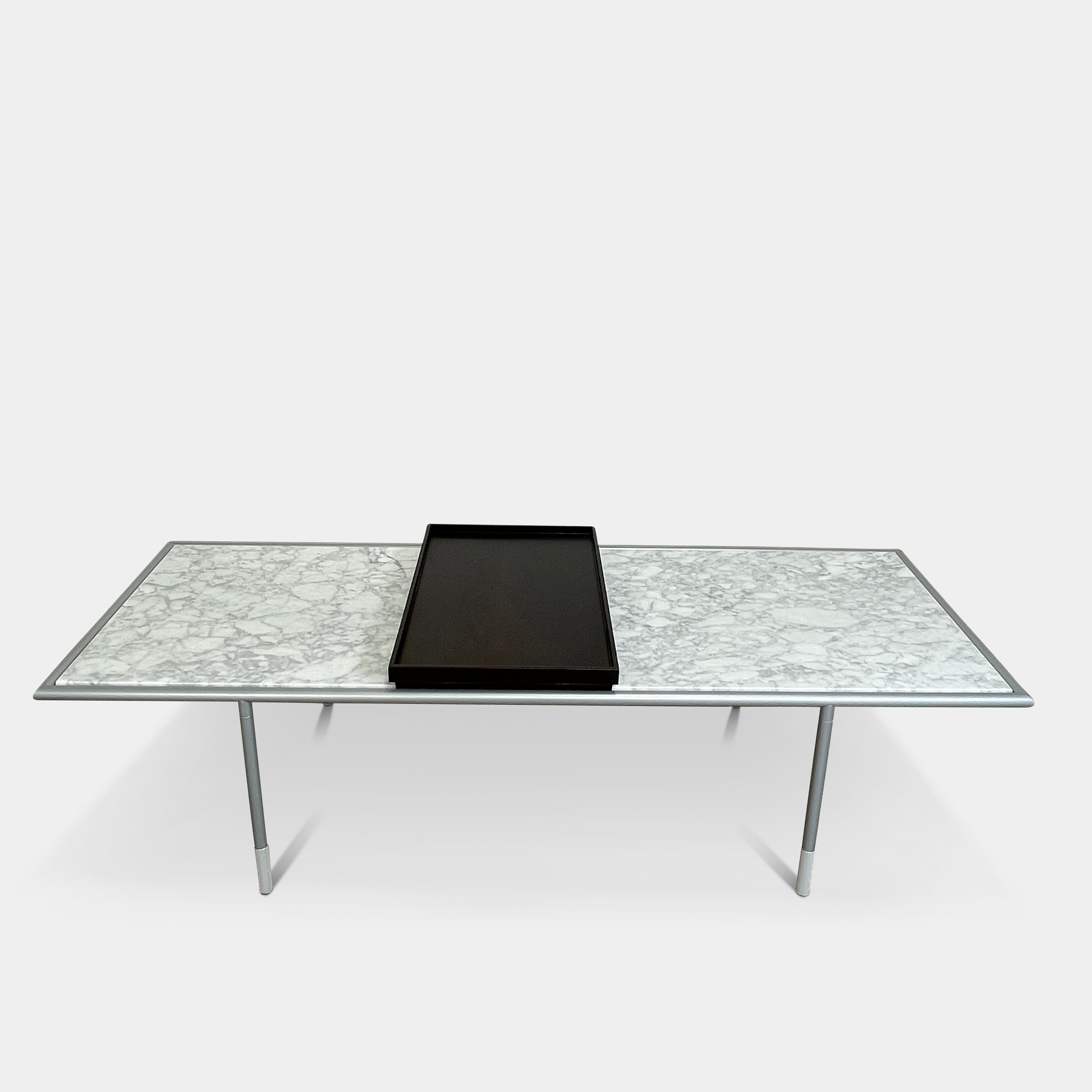 The Artelano Carrara Marble Coffee Table boasts a rectangular marble top with sleek metal legs and a central wood tray, exuding the Parisian elegance of the Artelano brand.