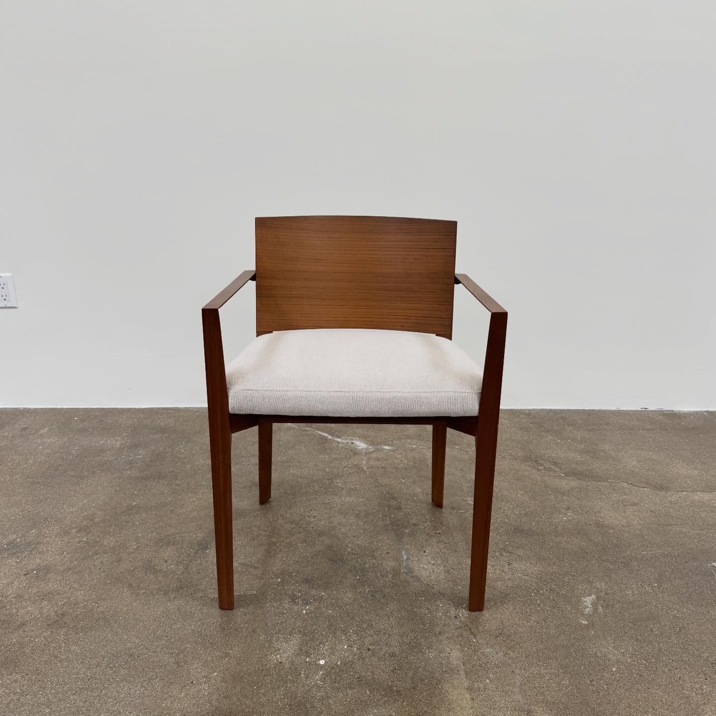 A set of 8 Porro Lario dining chairs by Porro, featuring minimalist armrests and light-cushioned seats, sits on a concrete floor against a plain white wall, reflecting refined contemporary style.