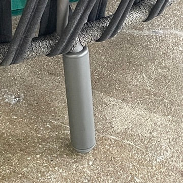 A Varaschin Outdoor Emma Cross Daybed in black with a green cushion and five assorted gray and black pillows rests on a concrete floor by a plain white wall.