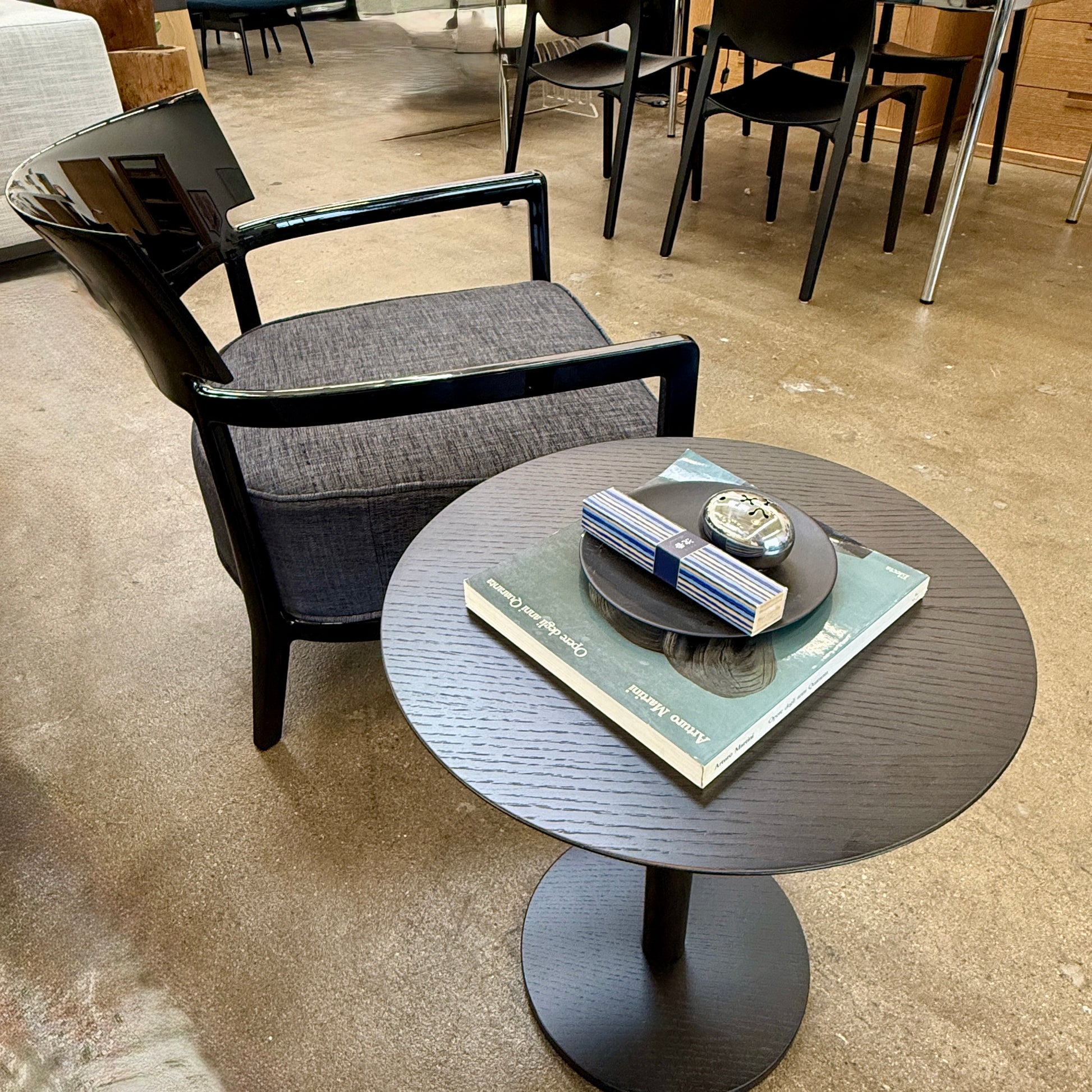 A Kartell Cara Lounge Chair by Kartell, featuring a wide black backrest and dark cushion, rests on a concrete floor in front of a plain white wall.