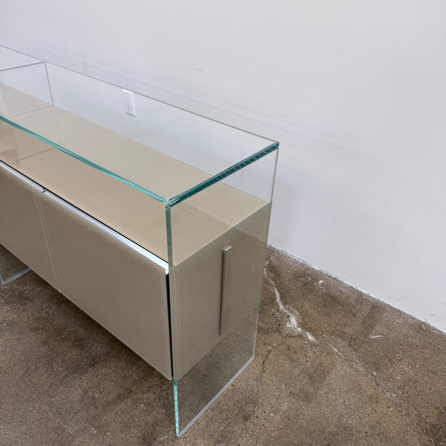 A long Gallotti & Radice Air Console Table featuring a clear glass frame and four opaque taupe storage cabinets.