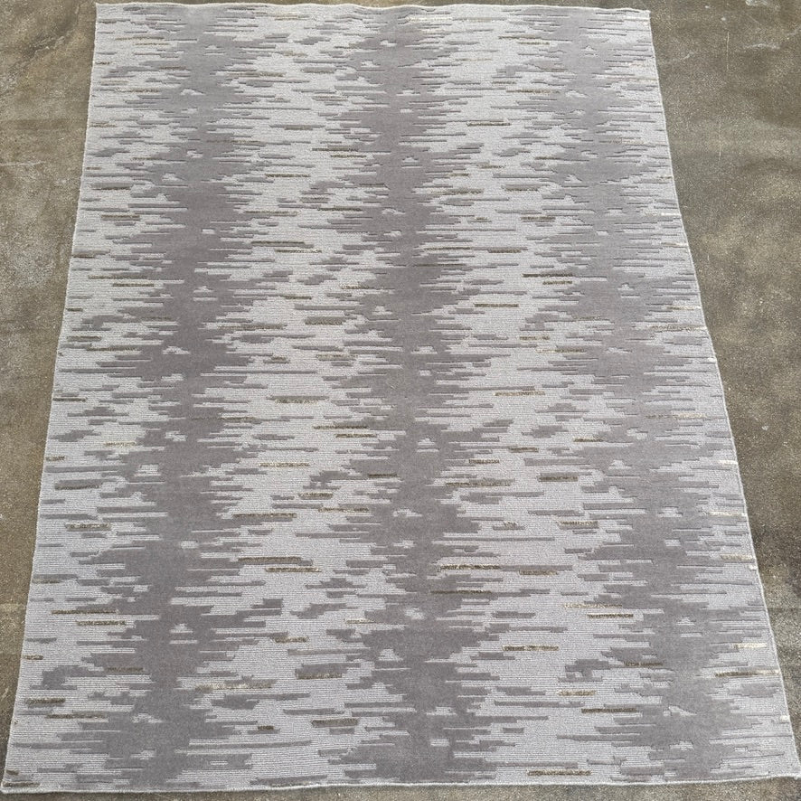 A close-up of the Kvadrat Multi-pile Wool and Silk Rug by Kvadrat, featuring an abstract linear pattern in light and dark gray wool and silk, displayed on a white background.