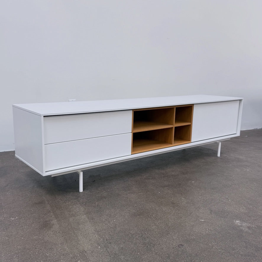 Low-profile white DWR Treku Aura Media Unit on thin legs, featuring two side cabinets and a central open shelf section with a wood-toned interior.