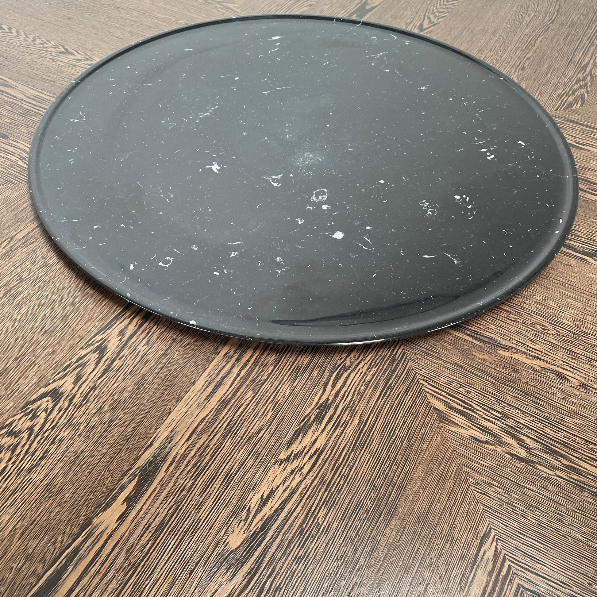 Round wooden table with a central raised circular platform and sleek black legs, reminiscent of the elegant design seen in the B&B Italia Alex Dining Table With Rotating Marble Tray. The rotating marble tray adds a refined touch, making it a versatile centerpiece on a white background.