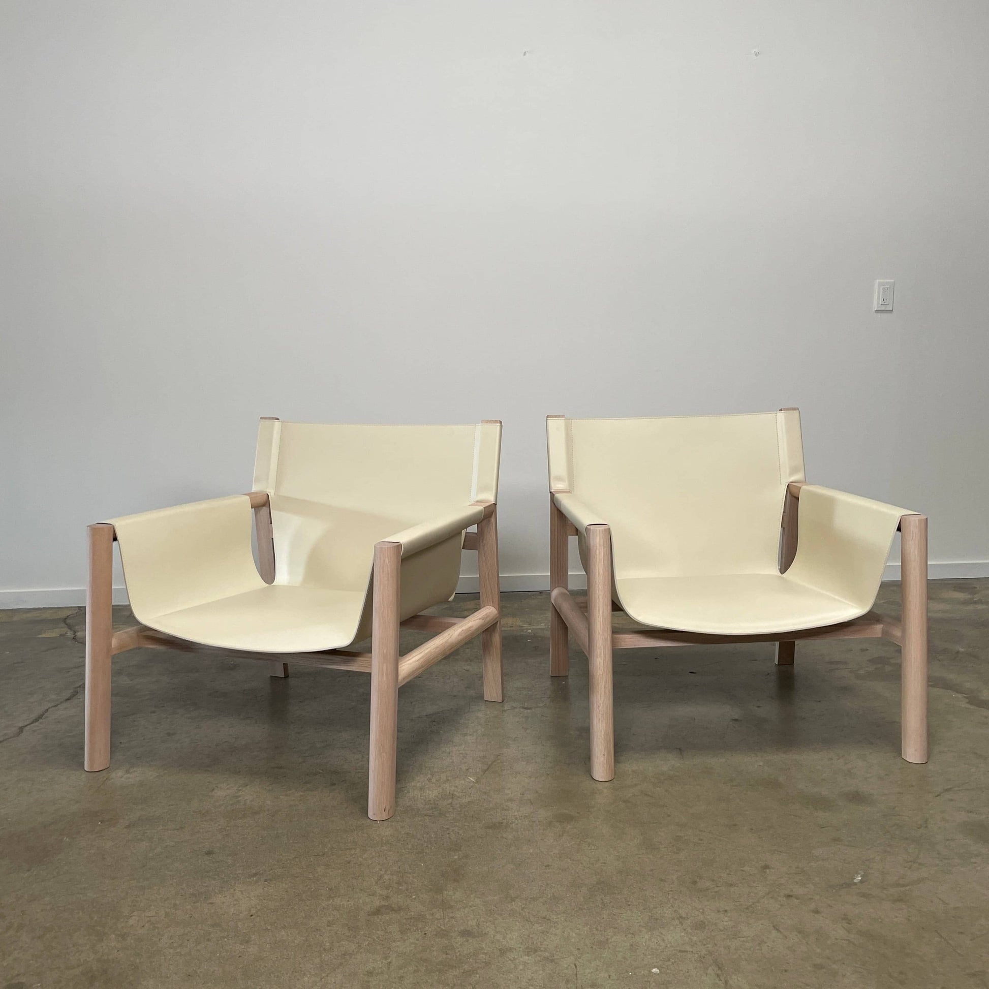 Introducing the B&B Italia Pablo Armchair, a minimalist beige chair with a wooden frame and wide seat from B&B Italia that features comfortable design elements. It rests on a concrete floor against a plain wall, inviting relaxation in its refined simplicity.