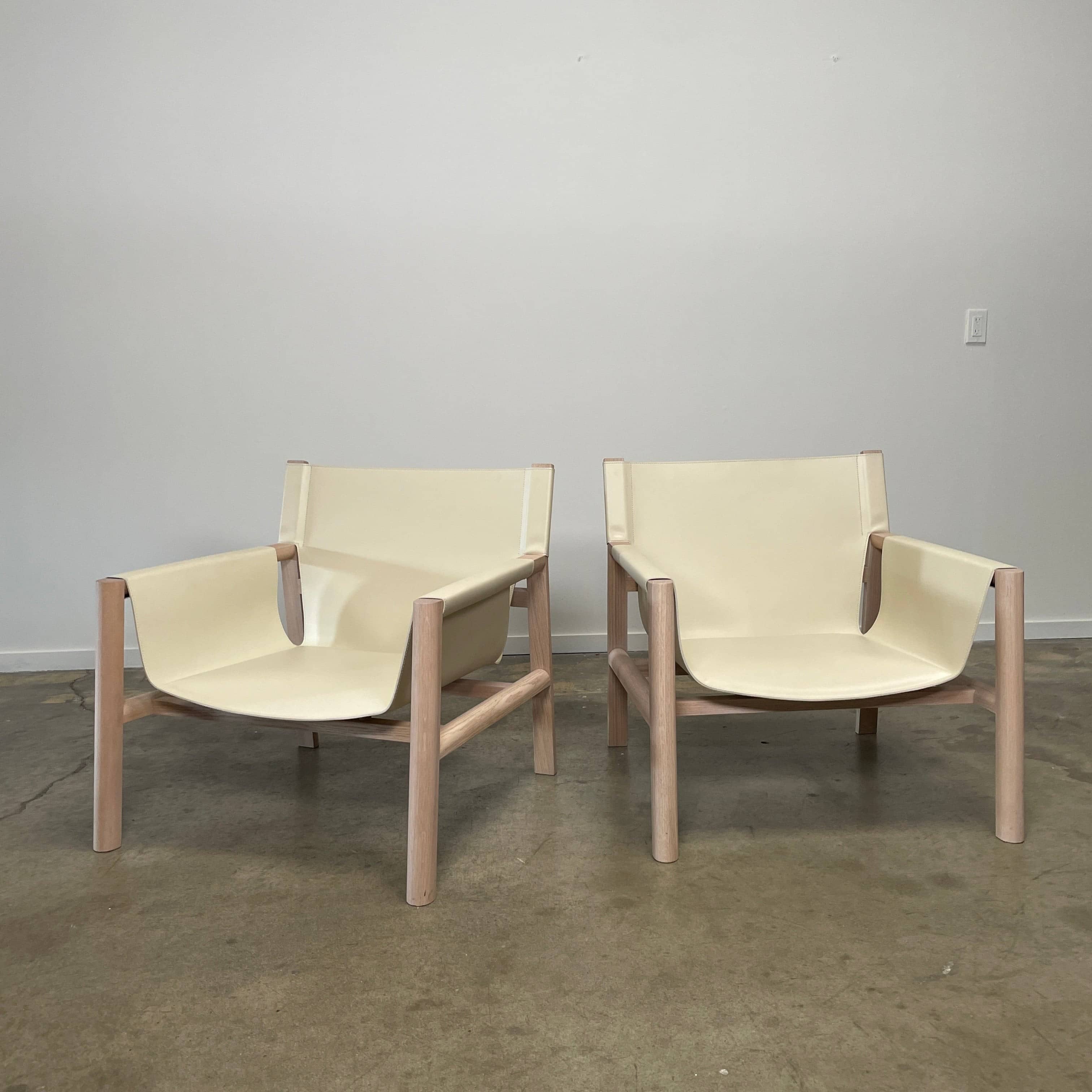 Introducing the B&B Italia Pablo Armchair, a minimalist beige chair with a wooden frame and wide seat from B&B Italia that features comfortable design elements. It rests on a concrete floor against a plain wall, inviting relaxation in its refined simplicity.