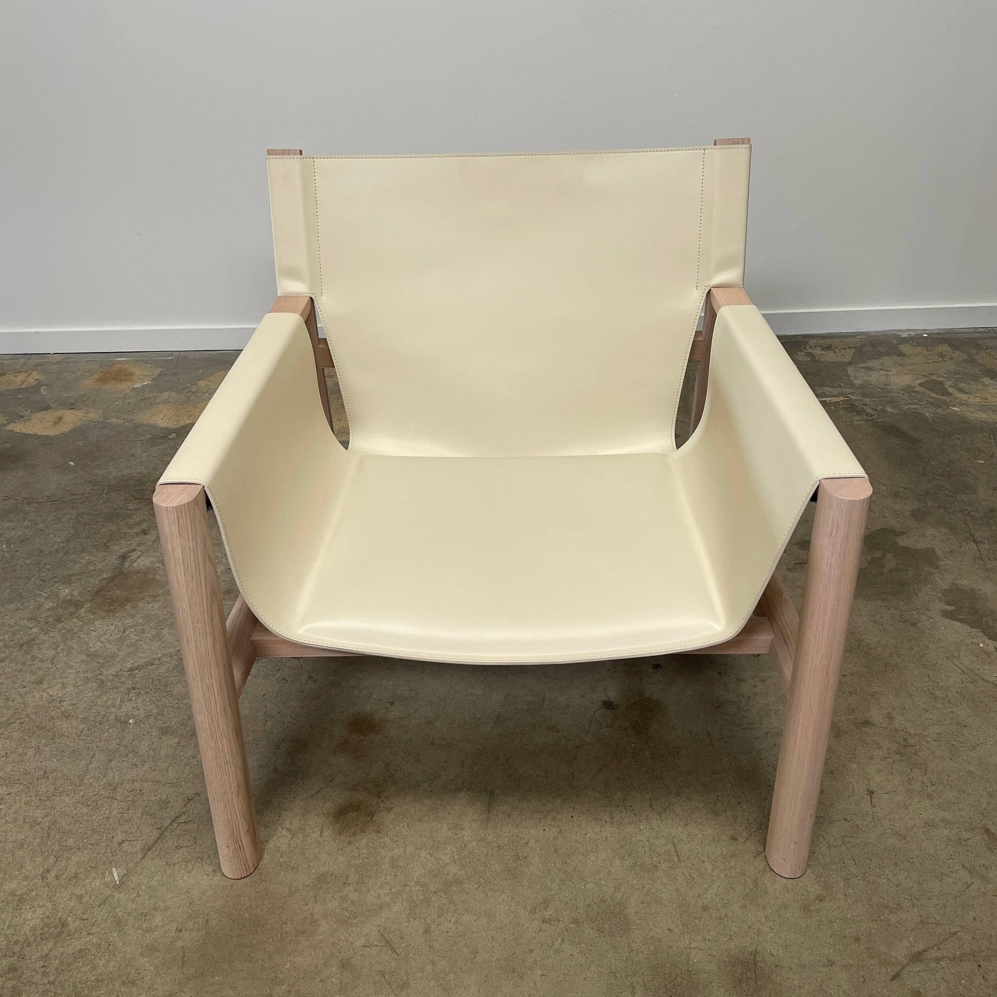 Introducing the B&B Italia Pablo Armchair, a minimalist beige chair with a wooden frame and wide seat from B&B Italia that features comfortable design elements. It rests on a concrete floor against a plain wall, inviting relaxation in its refined simplicity.