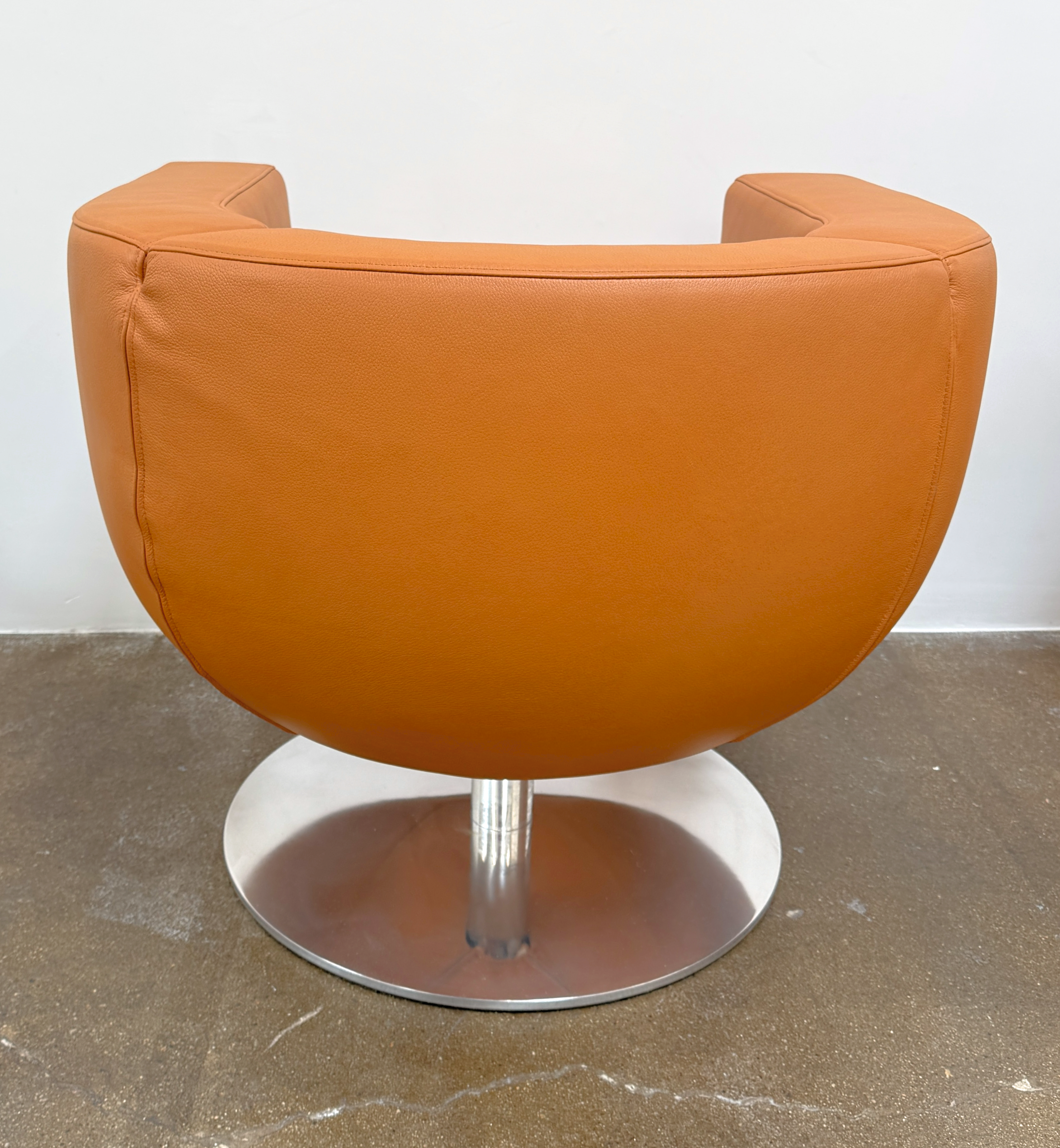 The B&B Italia Tulip Swivel Armchair by B&B Italia features a modern orange design with a curved backrest, seat cushion, and metal swivel base, shown against a plain white background.