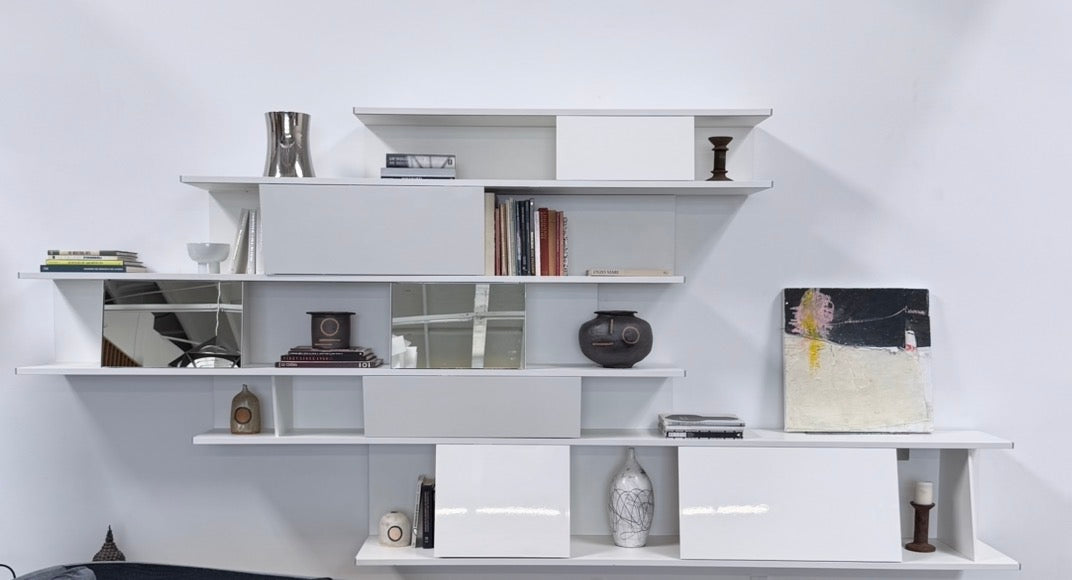 A white, wall-hanging B&B Italia Shift Wall Hanging Shelving System featuring horizontal tiers, enclosed cabinets, and assorted decorative objects and books to create a sculptured bookcase.