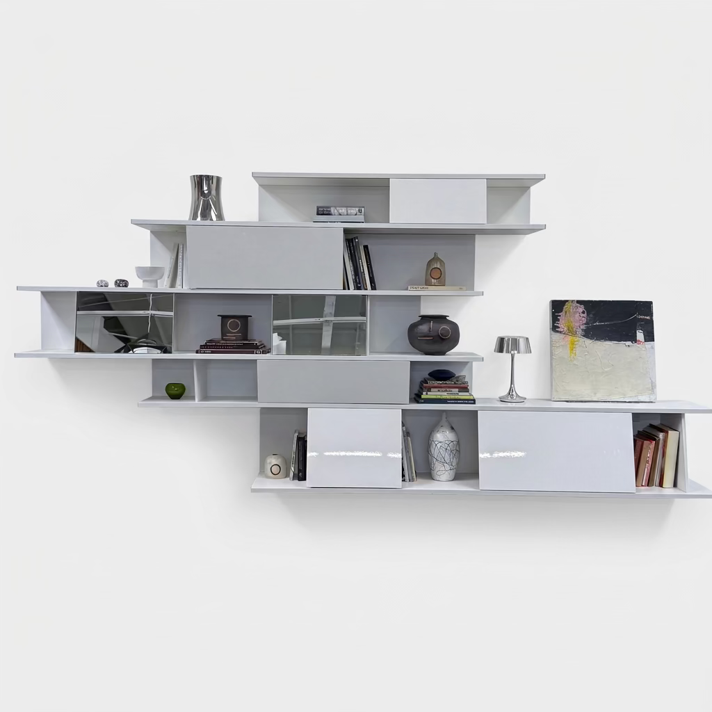 A white, wall-hanging B&B Italia Shift Wall Hanging Shelving System featuring horizontal tiers, enclosed cabinets, and assorted decorative objects and books to create a sculptured bookcase.