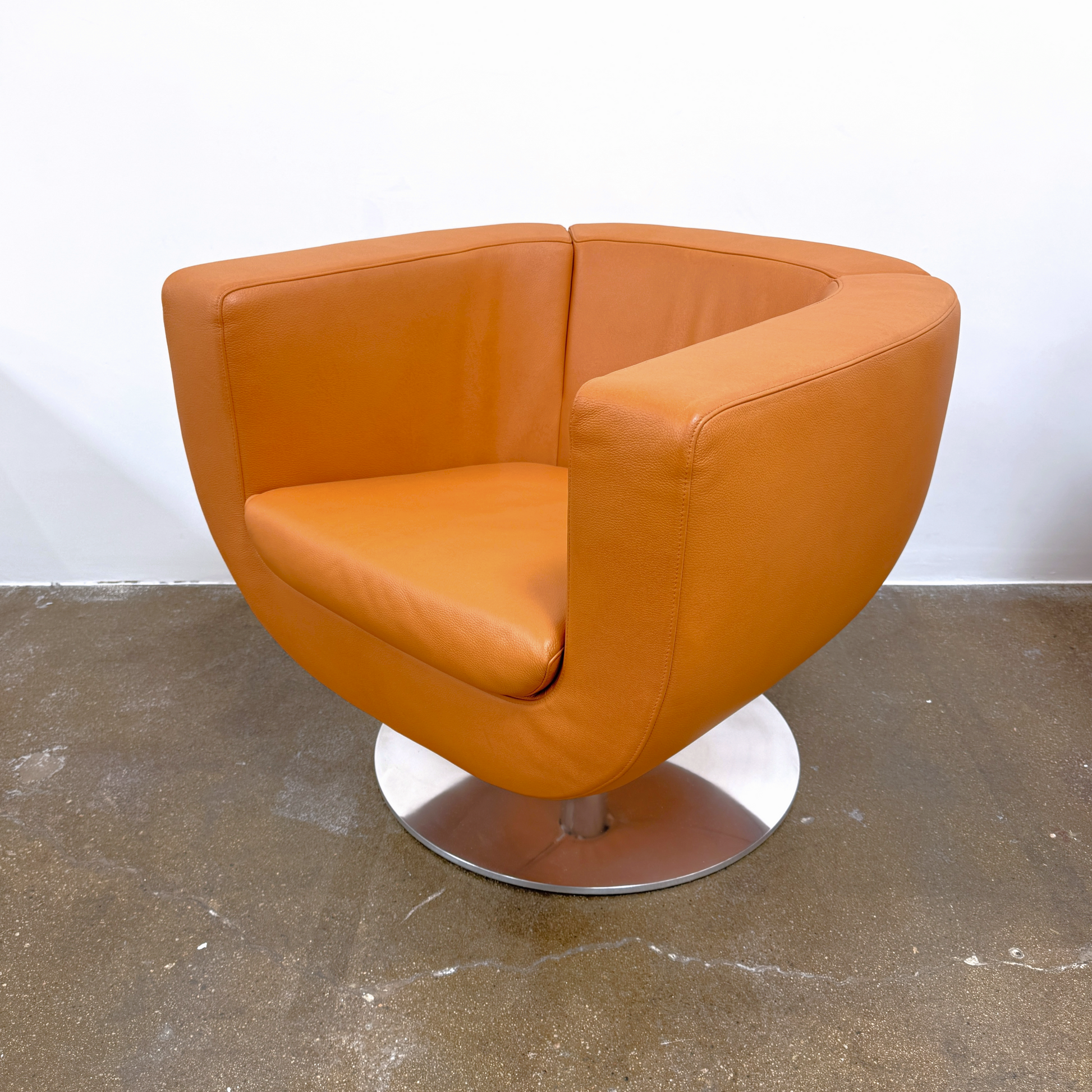 The B&B Italia Tulip Swivel Armchair by B&B Italia features a modern orange design with a curved backrest, seat cushion, and metal swivel base, shown against a plain white background.