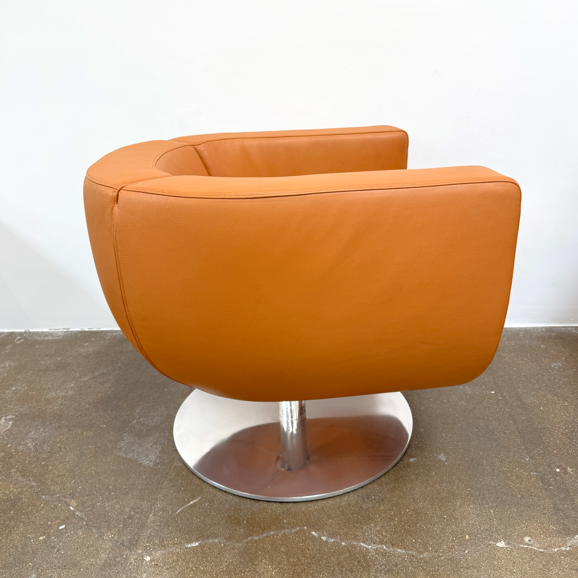 The B&B Italia Tulip Swivel Armchair by B&B Italia features a modern orange design with a curved backrest, seat cushion, and metal swivel base, shown against a plain white background.