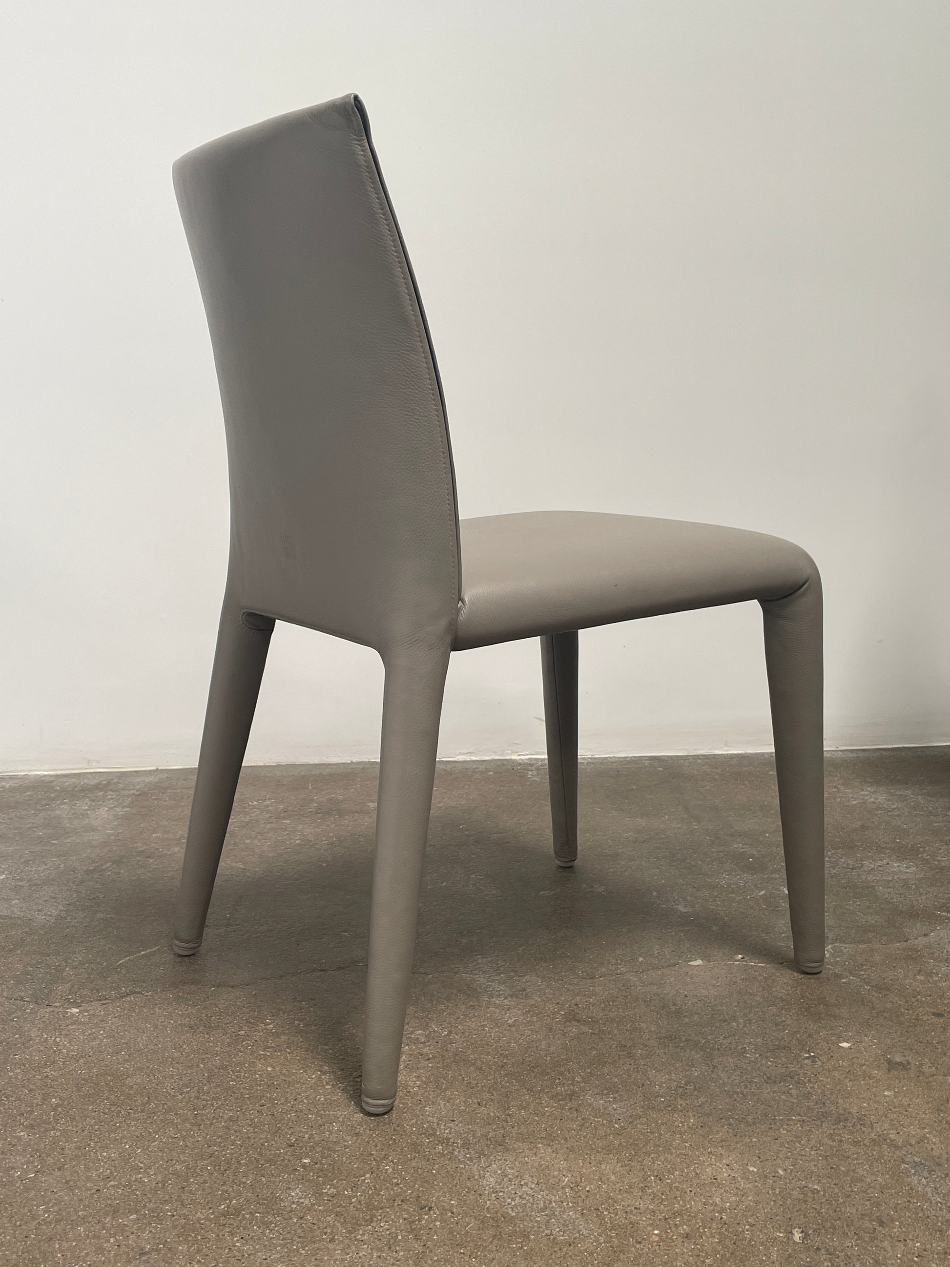 Six B&B Italia Vol au Vent Dining Chairs, embodying the elegance of Italian style, are arranged in two rows in an empty room with a concrete floor and a plain white wall.