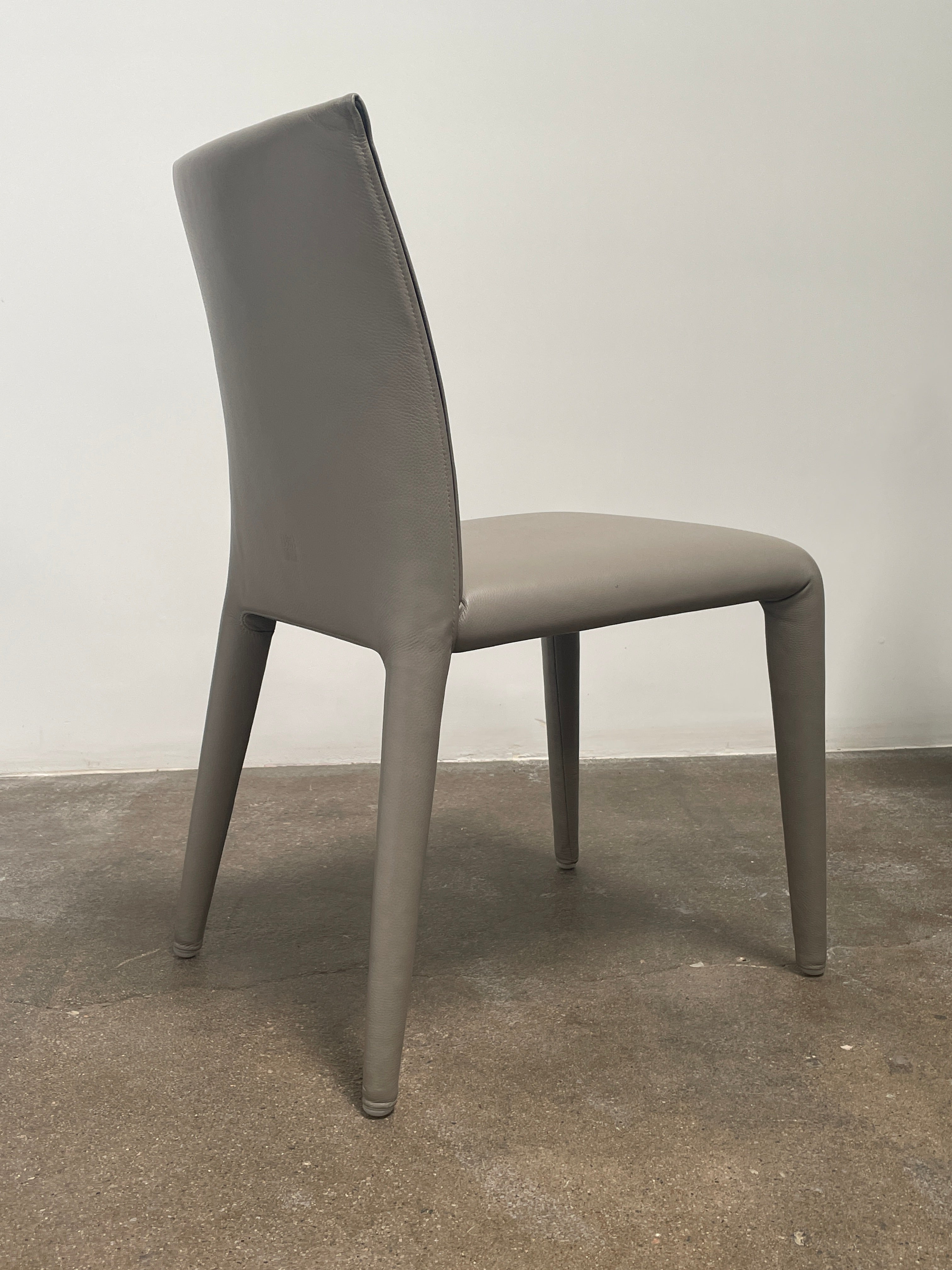 Six B&B Italia Vol au Vent Dining Chairs, embodying the elegance of Italian style, are arranged in two rows in an empty room with a concrete floor and a plain white wall.