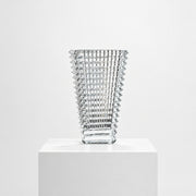 The Baccarat Eye Vase by Baccarat features clear glass with a geometric textured design, shown on a white pedestal and plain white background.