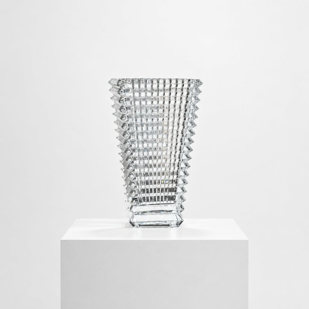 The Baccarat Eye Vase by Baccarat features clear glass with a geometric textured design, shown on a white pedestal and plain white background.