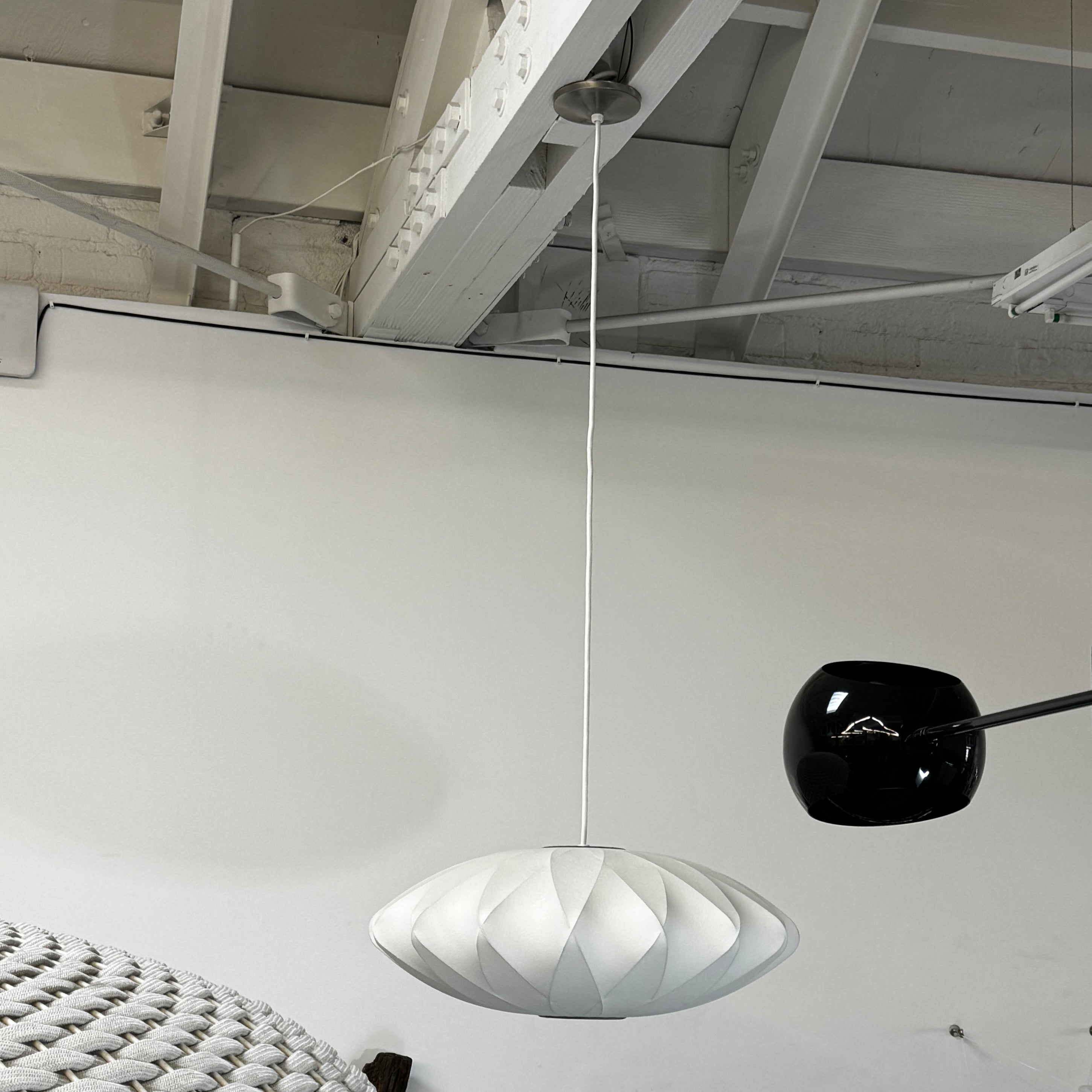 A medium Herman Miller Nelson Saucer Crisscross Bubble Pendant in white hangs before a wooden slat partition and beige sofa.