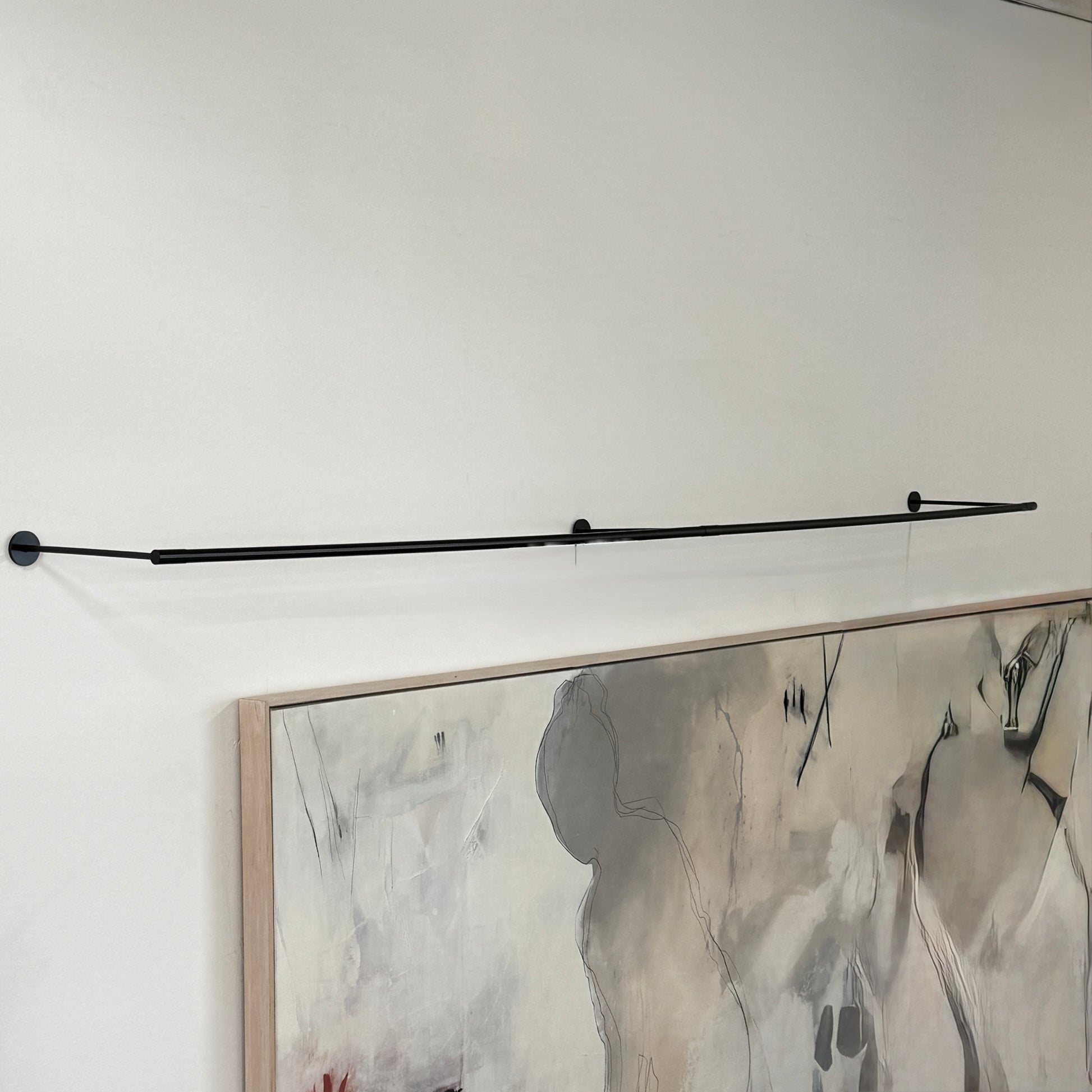 A modern abstract painting hangs on a white wall above a desk, illuminated by the Juniper THIN System Linear Light Wall-mounted from Juniper, with a lamp, documents, and office supplies arranged on the glass desktop.
