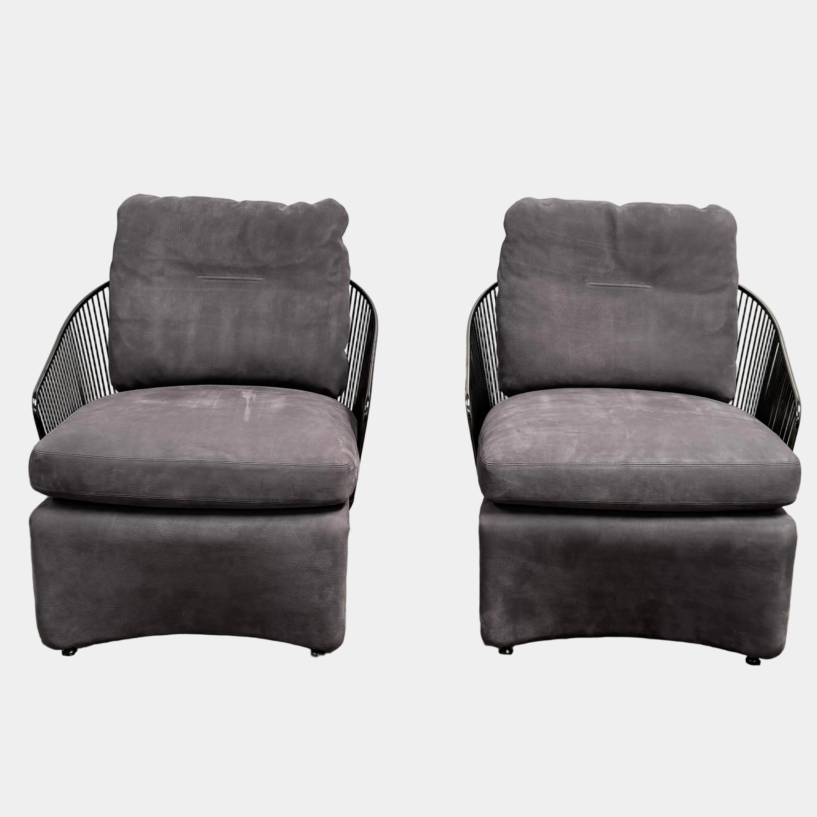 A set of two Minotti Colette Lounge Chairs by Minotti is displayed side by side against a plain white background. Each chair showcases luxurious gray nubuck leather upholstery and sleek black metal armrests, elegantly capturing the timeless mid-century silhouette characteristic of the iconic design.