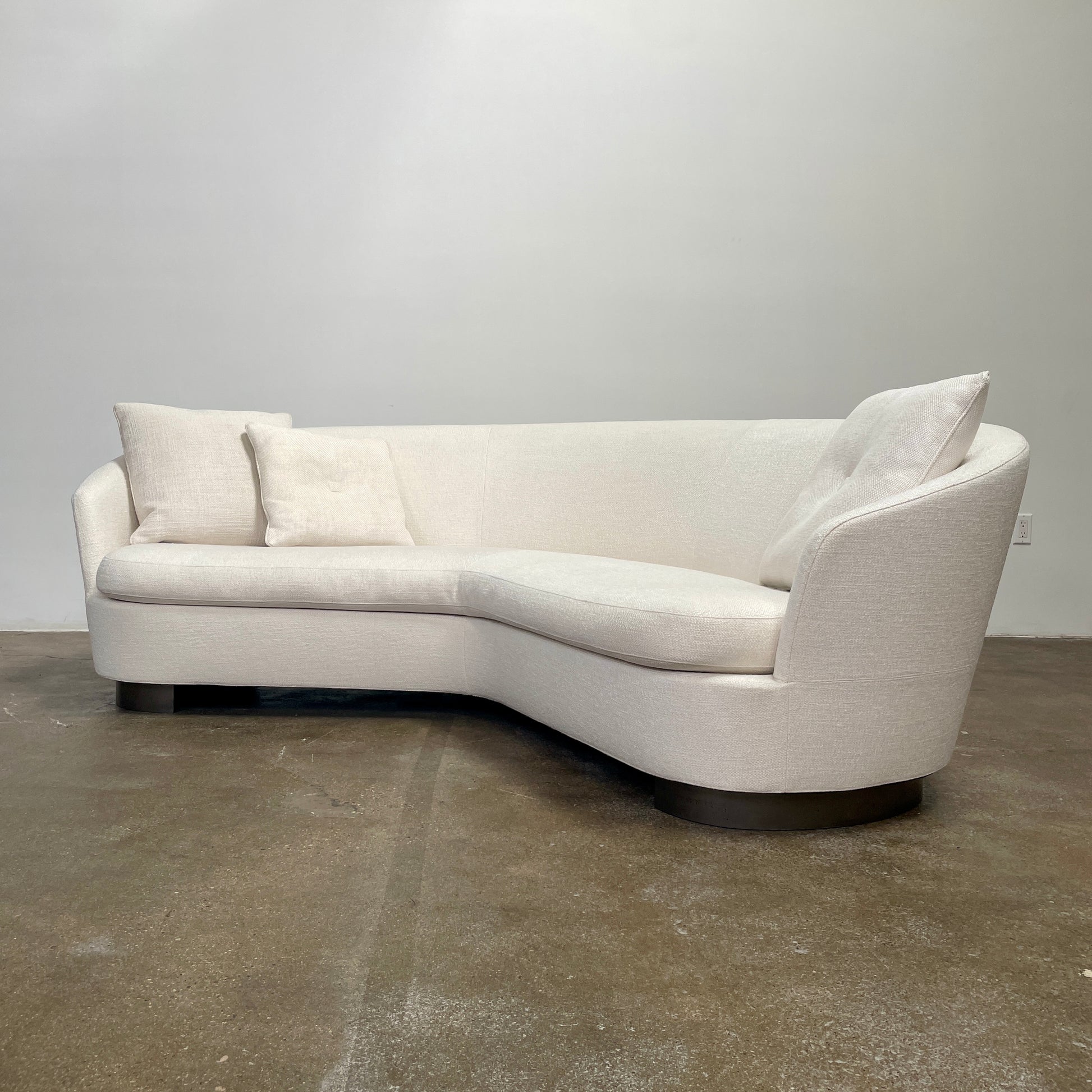 A Minotti Jacques Curved Sofa in white, featuring a contemporary design with curved lines and accompanied by two matching pillows, stands against a neutral background.