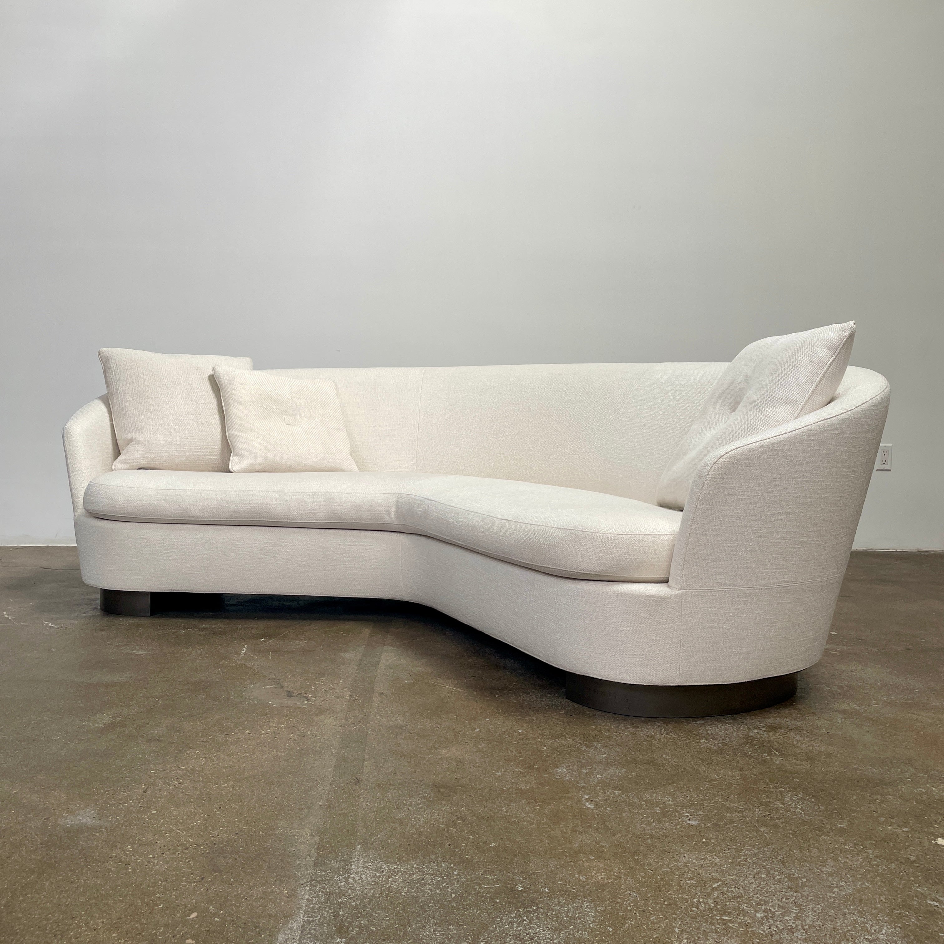 A Minotti Jacques Curved Sofa in white, featuring a contemporary design with curved lines and accompanied by two matching pillows, stands against a neutral background.