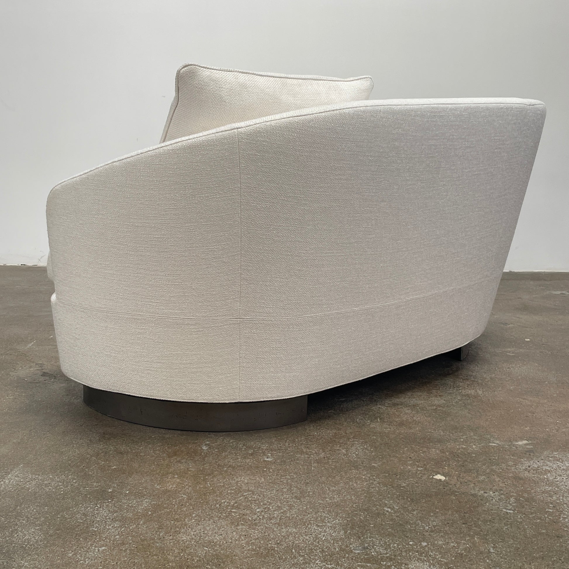 A Minotti Jacques Curved Sofa in white, featuring a contemporary design with curved lines and accompanied by two matching pillows, stands against a neutral background.