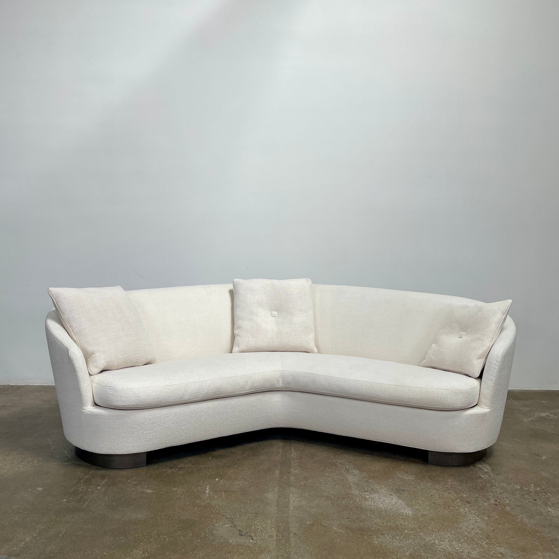 A Minotti Jacques Curved Sofa in white, featuring a contemporary design with curved lines and accompanied by two matching pillows, stands against a neutral background.