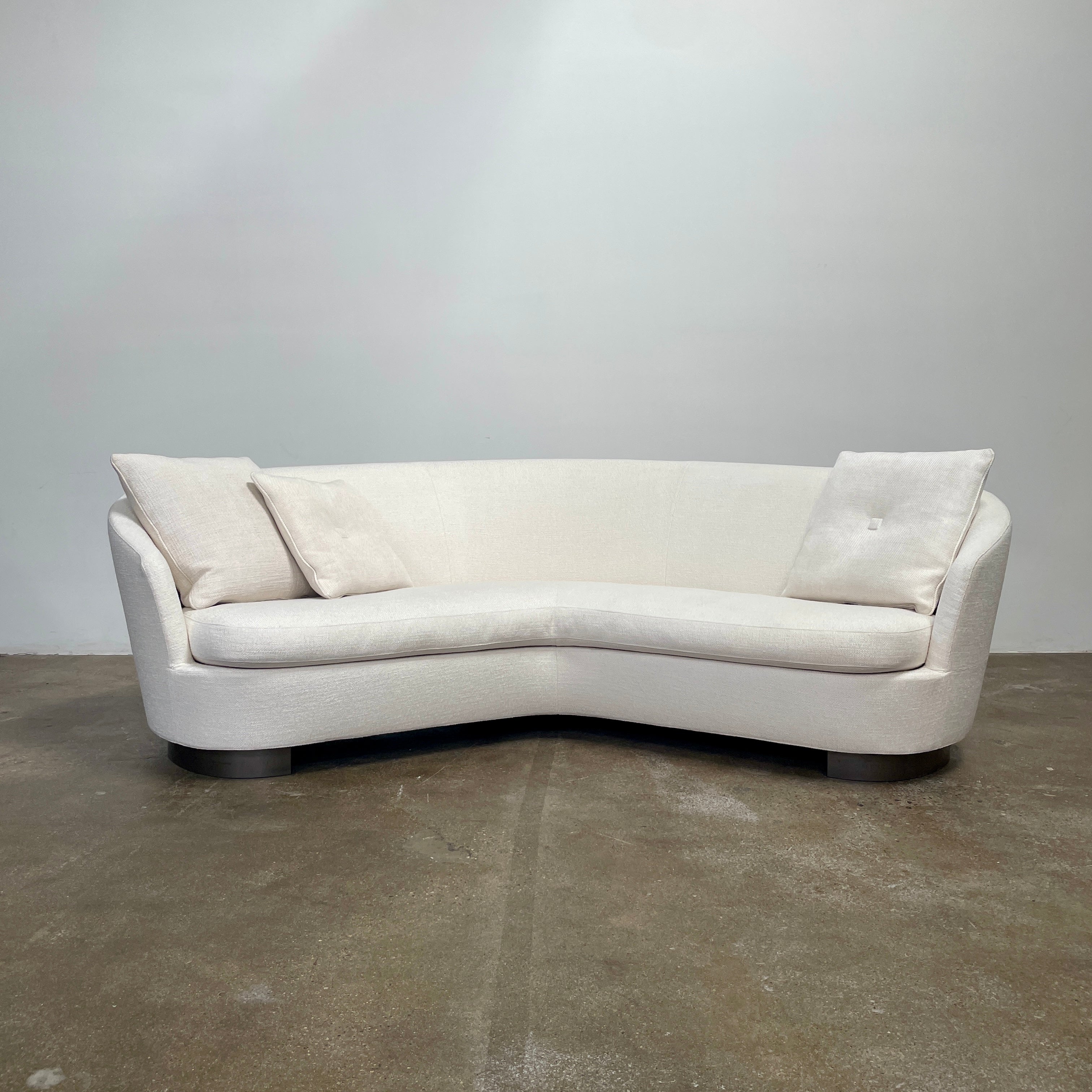 A Minotti Jacques Curved Sofa in white, featuring a contemporary design with curved lines and accompanied by two matching pillows, stands against a neutral background.