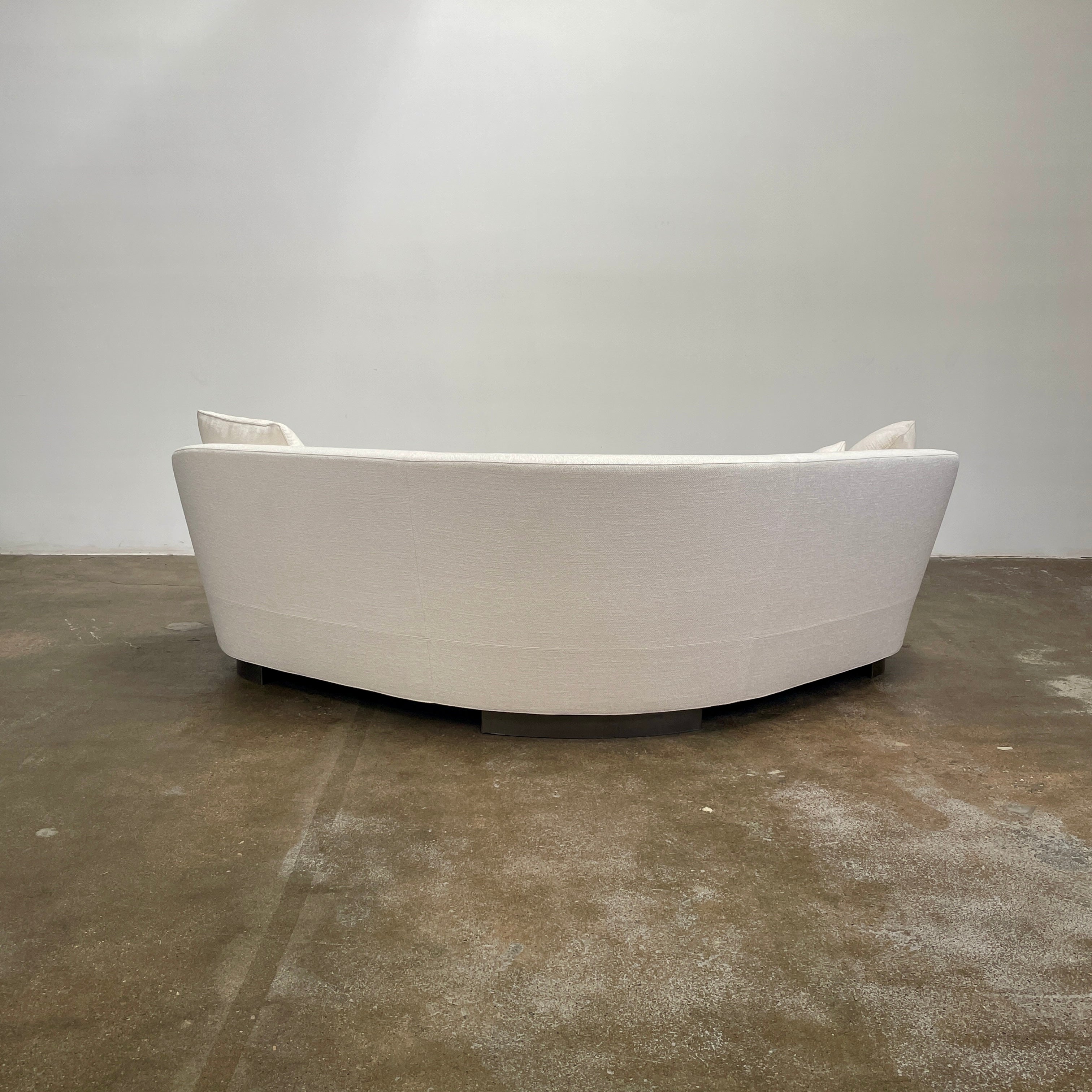 A Minotti Jacques Curved Sofa in white, featuring a contemporary design with curved lines and accompanied by two matching pillows, stands against a neutral background.