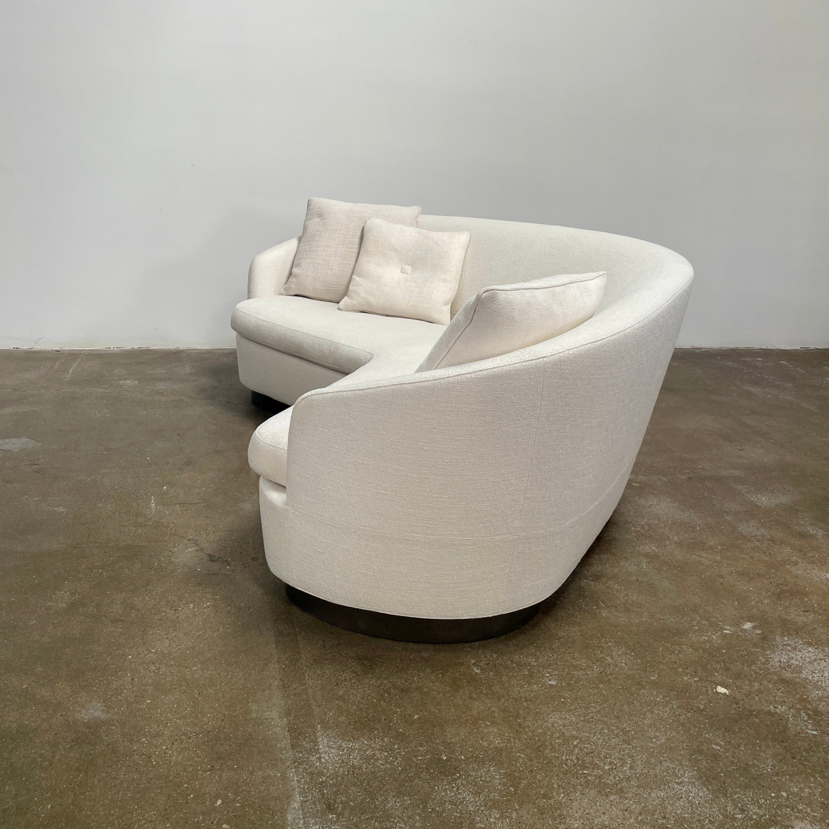 A Minotti Jacques Curved Sofa in white, featuring a contemporary design with curved lines and accompanied by two matching pillows, stands against a neutral background.