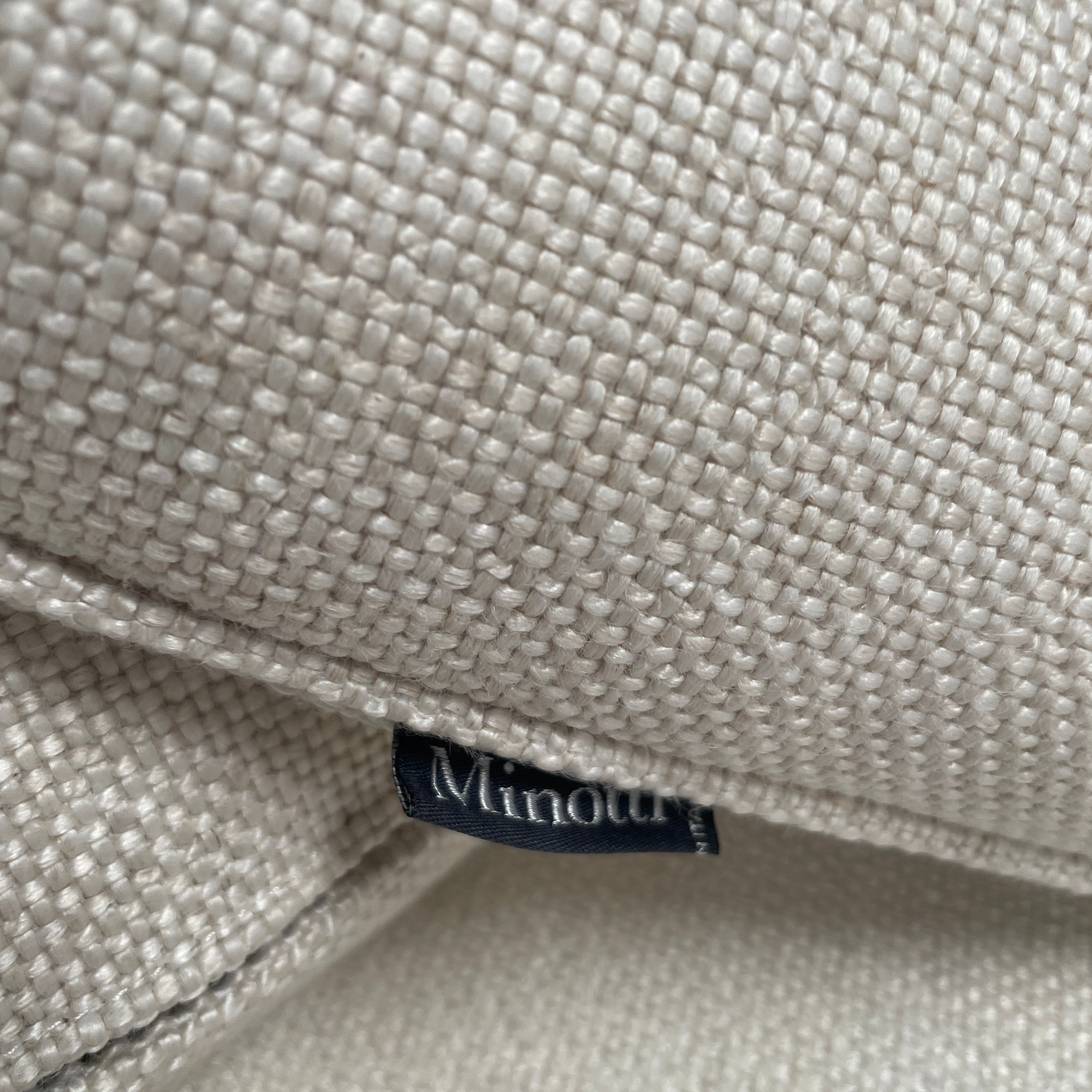 A Minotti Jacques Curved Sofa in white, featuring a contemporary design with curved lines and accompanied by two matching pillows, stands against a neutral background.