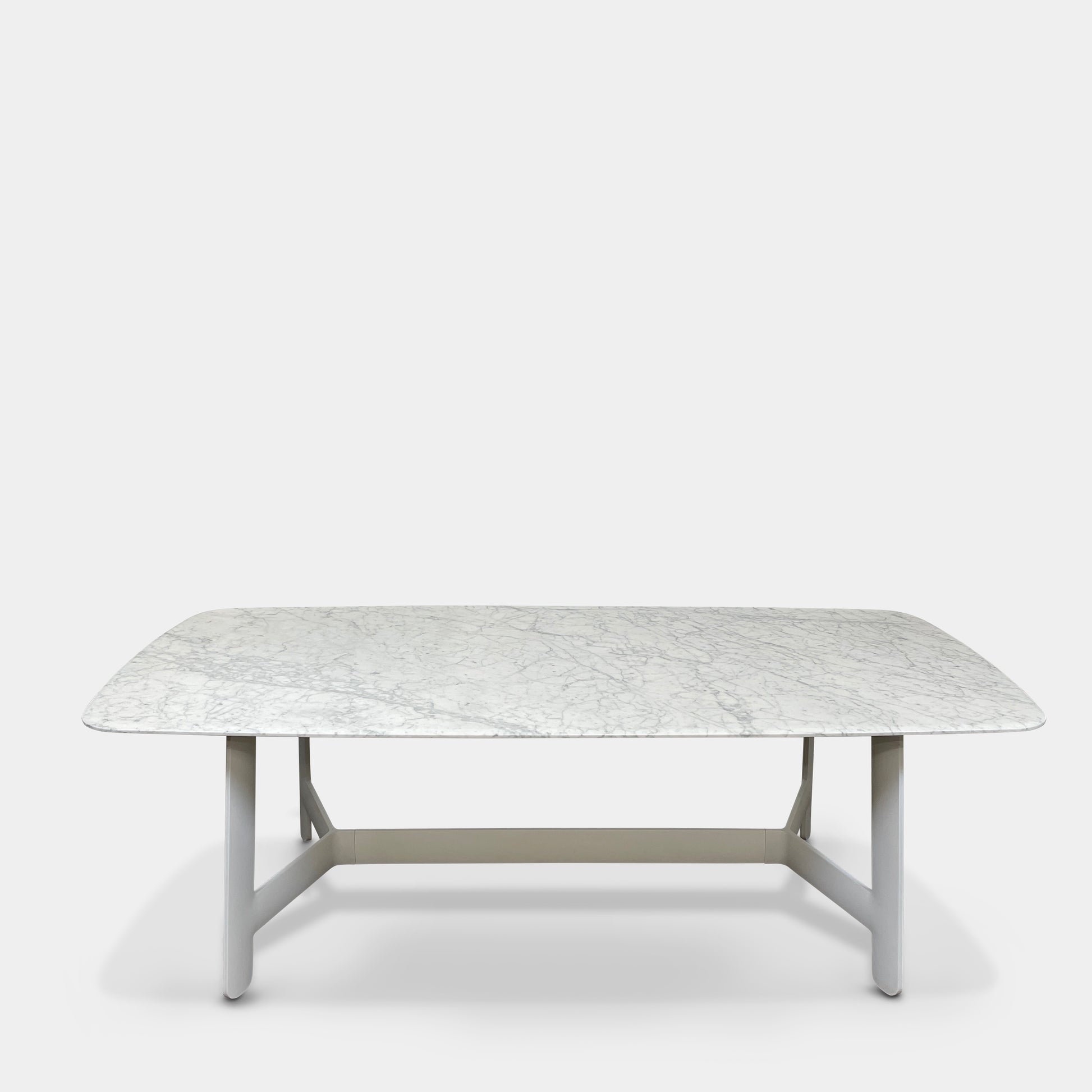 On a concrete floor against a plain white wall stands the B&B Italia Matte Carrara Marble Alex Dining Table, showcasing contemporary design with its long, rectangular form and white base, adding both style and sophistication to the space.