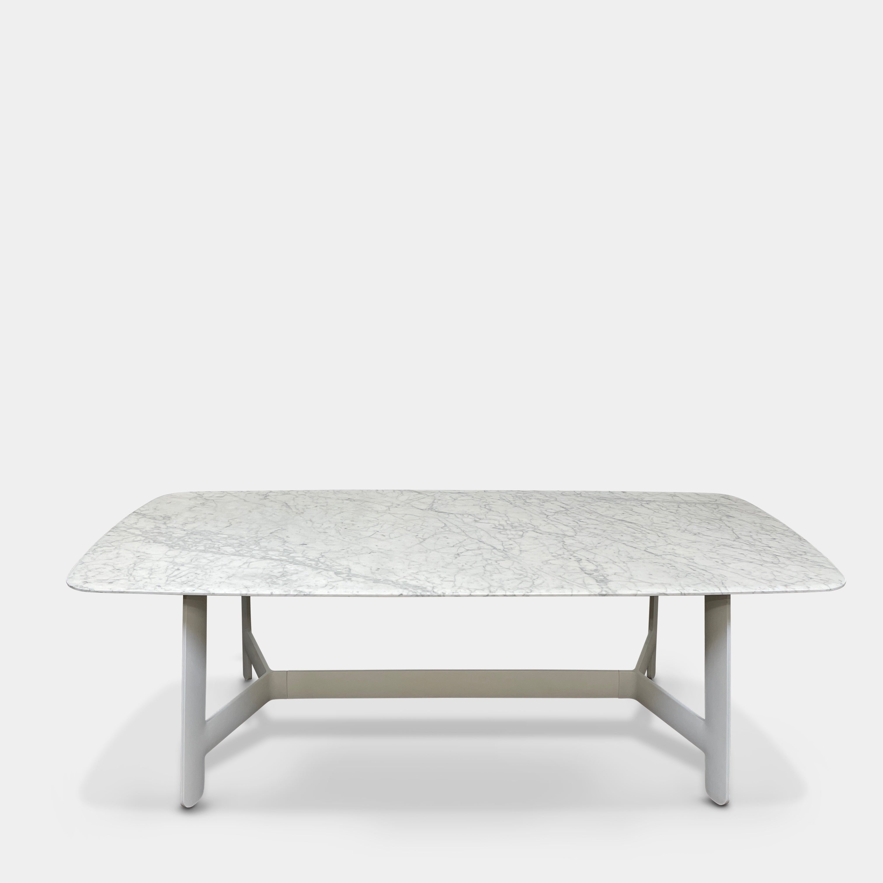 On a concrete floor against a plain white wall stands the B&B Italia Matte Carrara Marble Alex Dining Table, showcasing contemporary design with its long, rectangular form and white base, adding both style and sophistication to the space.