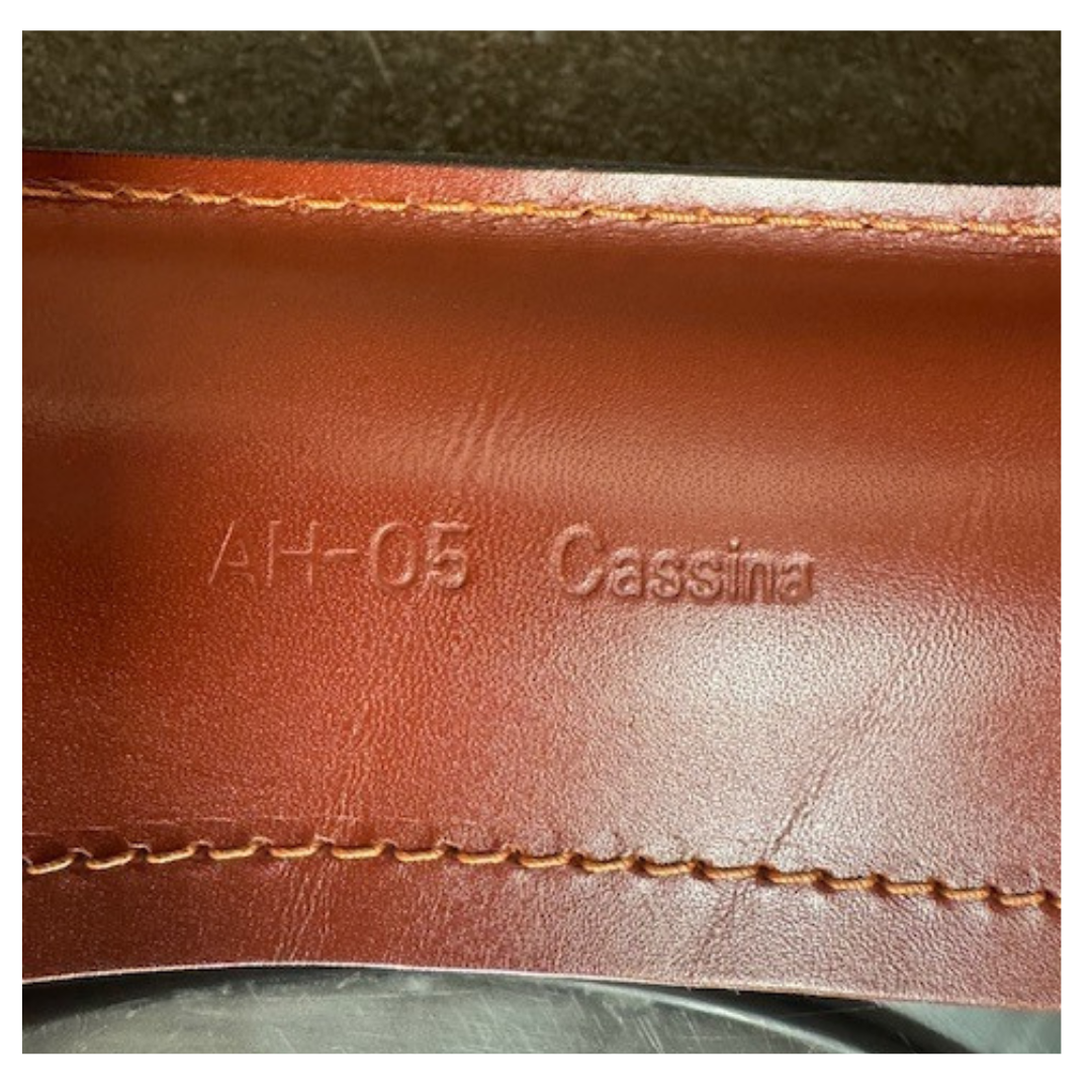 A red leather armchair, the Cassina Cab 413, drawing inspiration from the iconic Cab Chair with clean lines and a minimalist design, set against a plain grey background.