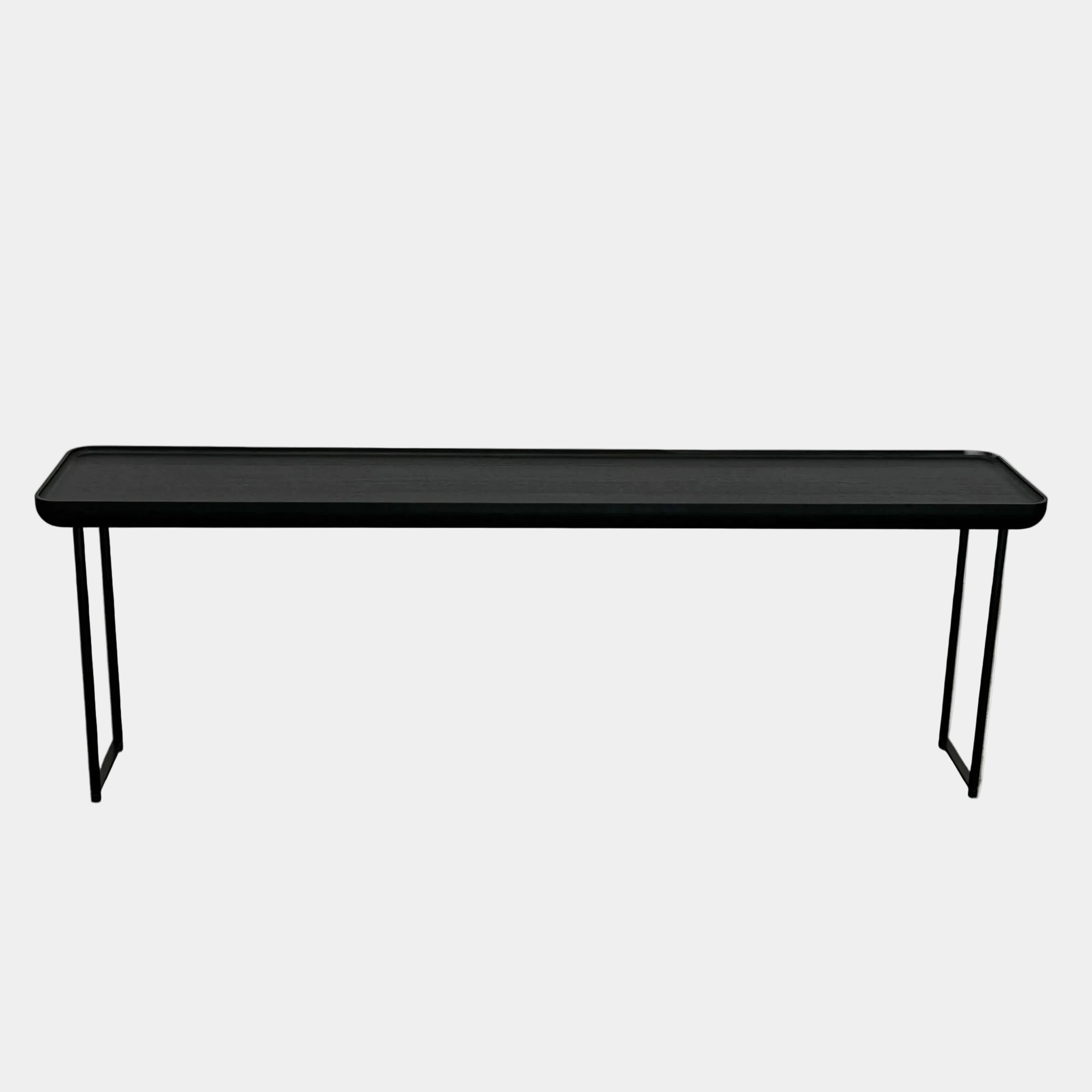 A minimalist black bench with a rectangular seat and slim metal legs echoes the elegant design of the Cassina Torei Occasional Table in Black Ash by Cassina, displayed against a plain white background.
