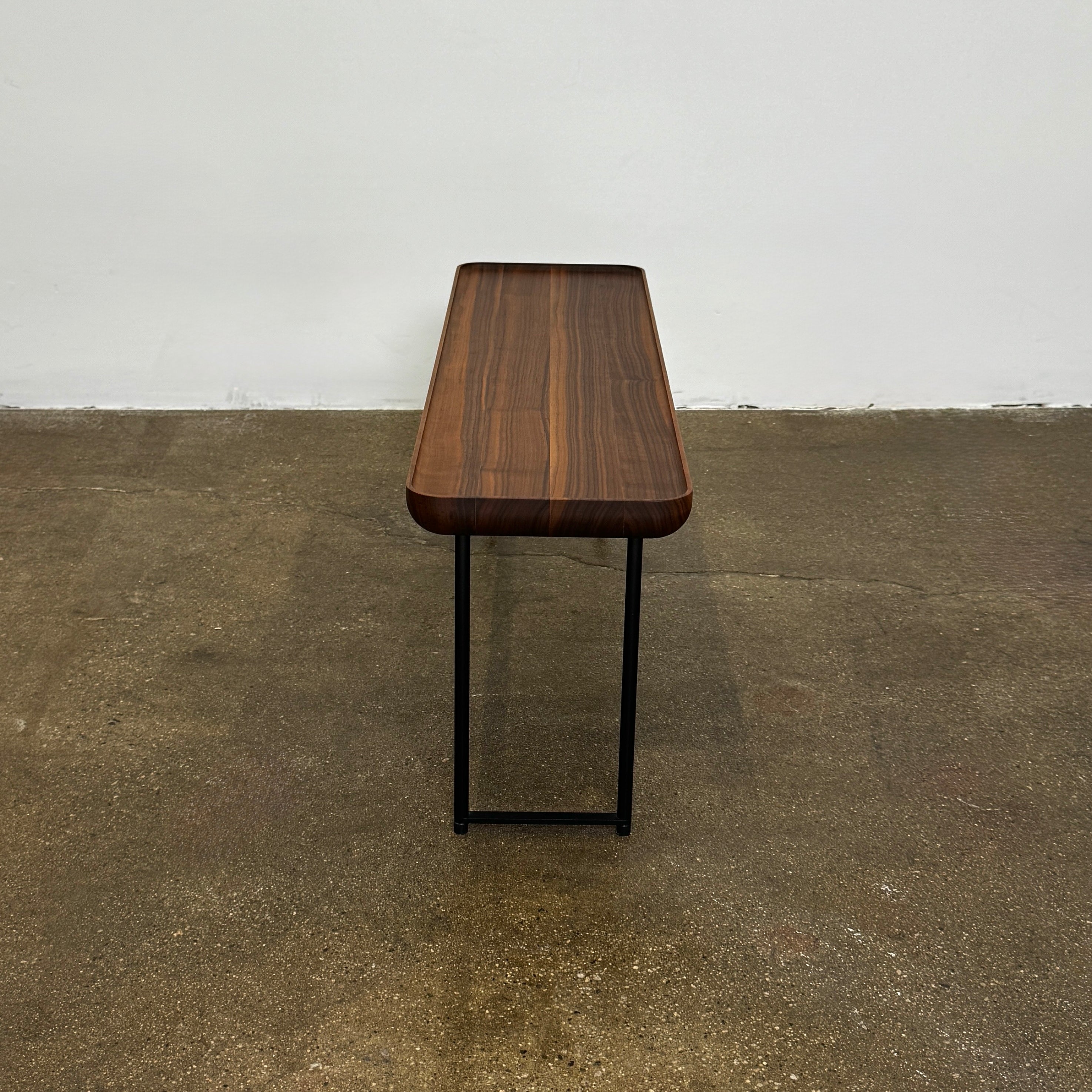 The Cassina Torei Occasional Table in Walnut by Cassina features rounded edges and sleek black metal legs, shown on a plain white background.