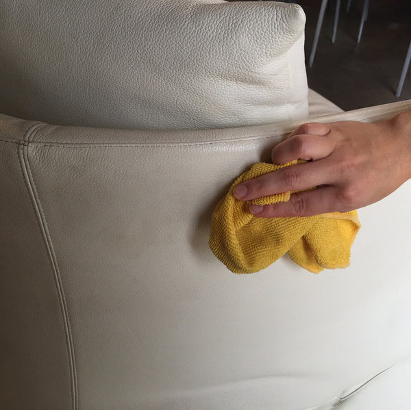 A person cleaning a white couch with a yellow cloth.