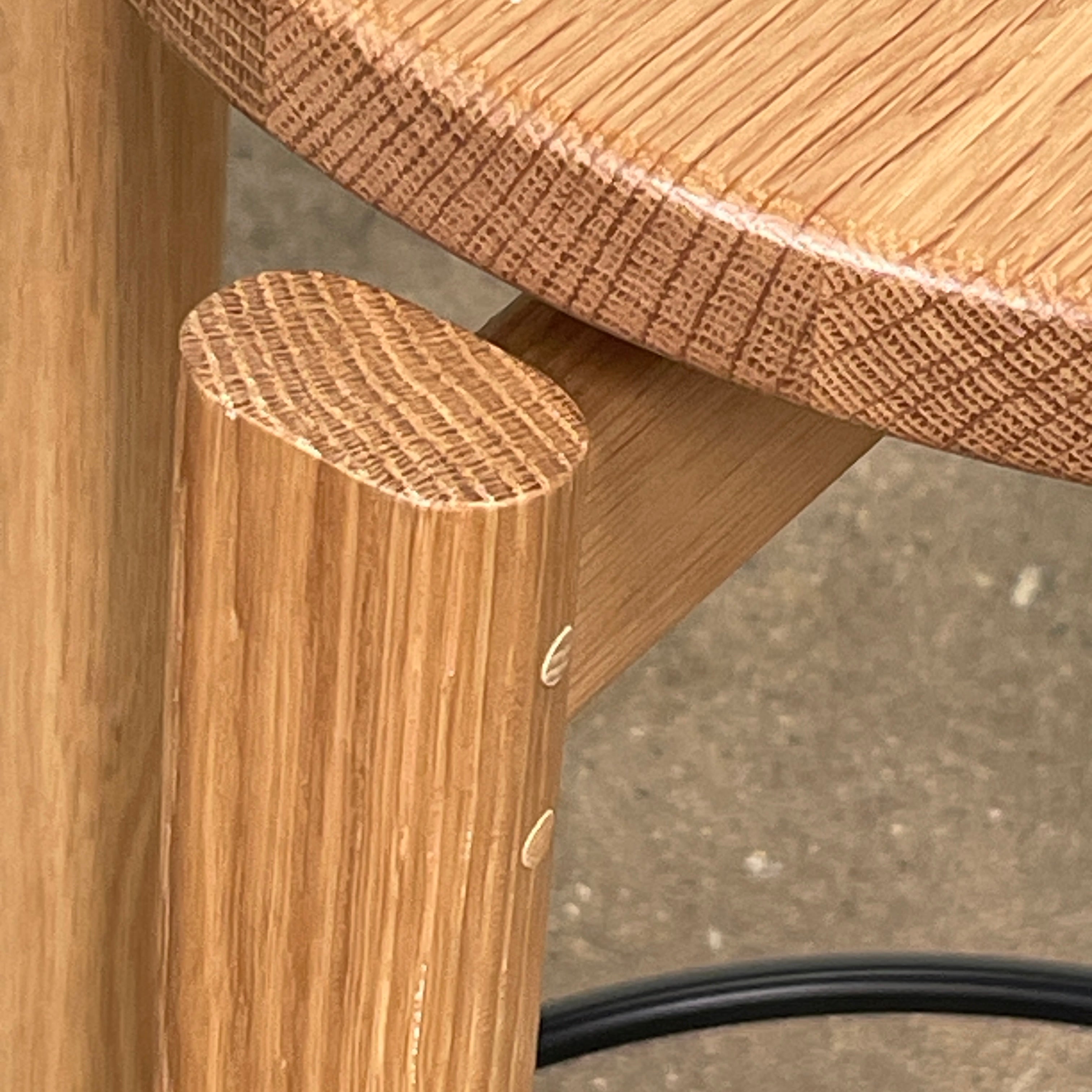 Audo Passage Bar Stools by Audo—two solid oak stools with round seats, three legs, and a black circular metal footrest—highlight Danish craftsmanship, shown against a plain white background.