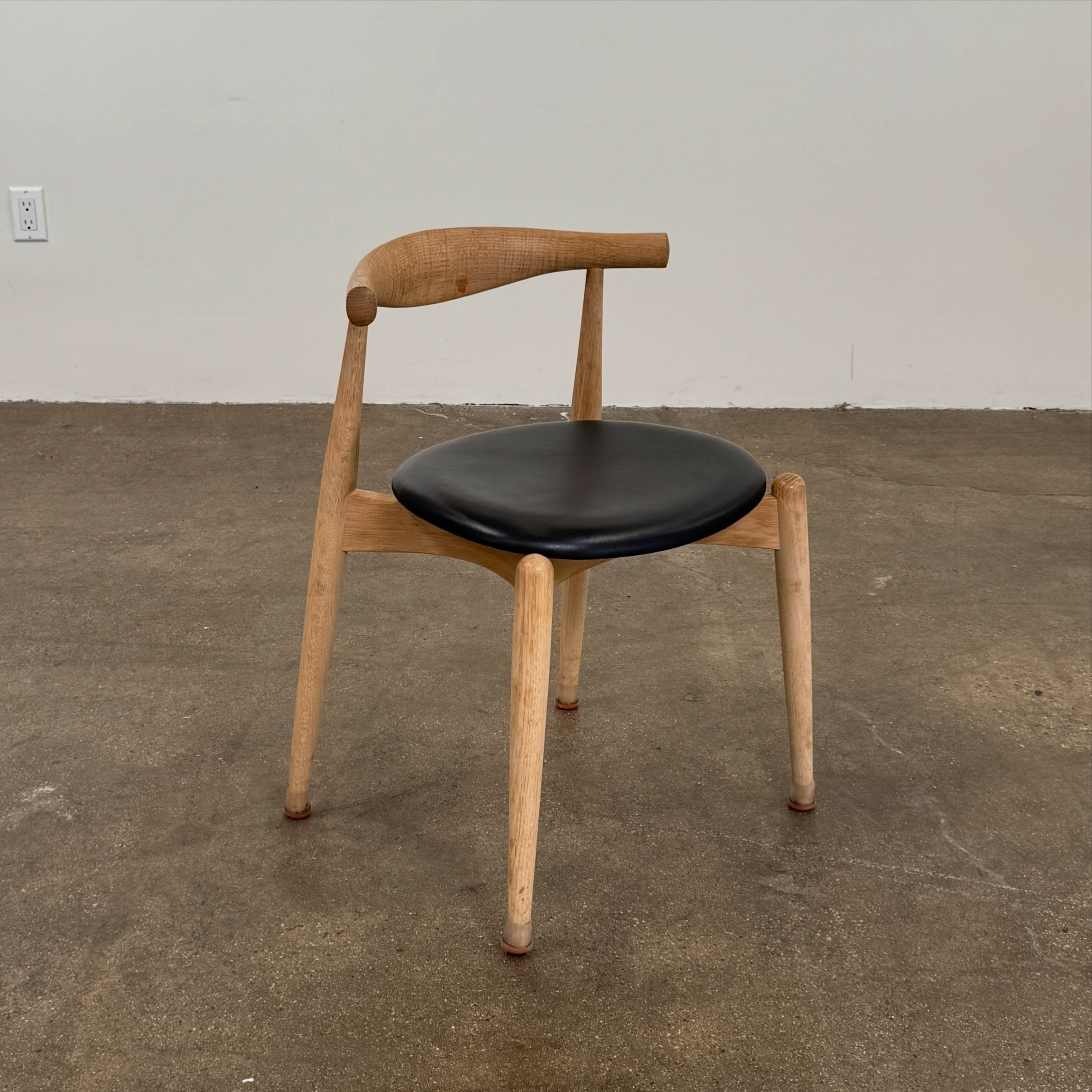 A set of five Carl Hansen & Son CH20 Elbow Chairs by Carl Hansen & Son, each with a curved wooden backrest and a round black seat cushion, are arranged in two rows against a plain white background.
