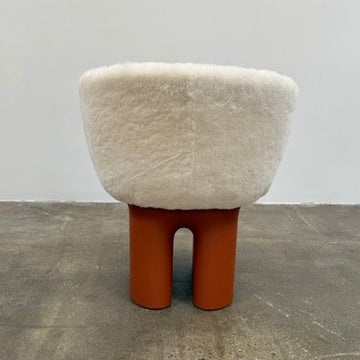 The Louis Vuitton Dolls Fur by Raw Edges is a modern chair with a curved white fluffy leather and fur seat, two short cylindrical brown legs, and a matching brown base, designed by Louis Vuitton and set against a plain background.