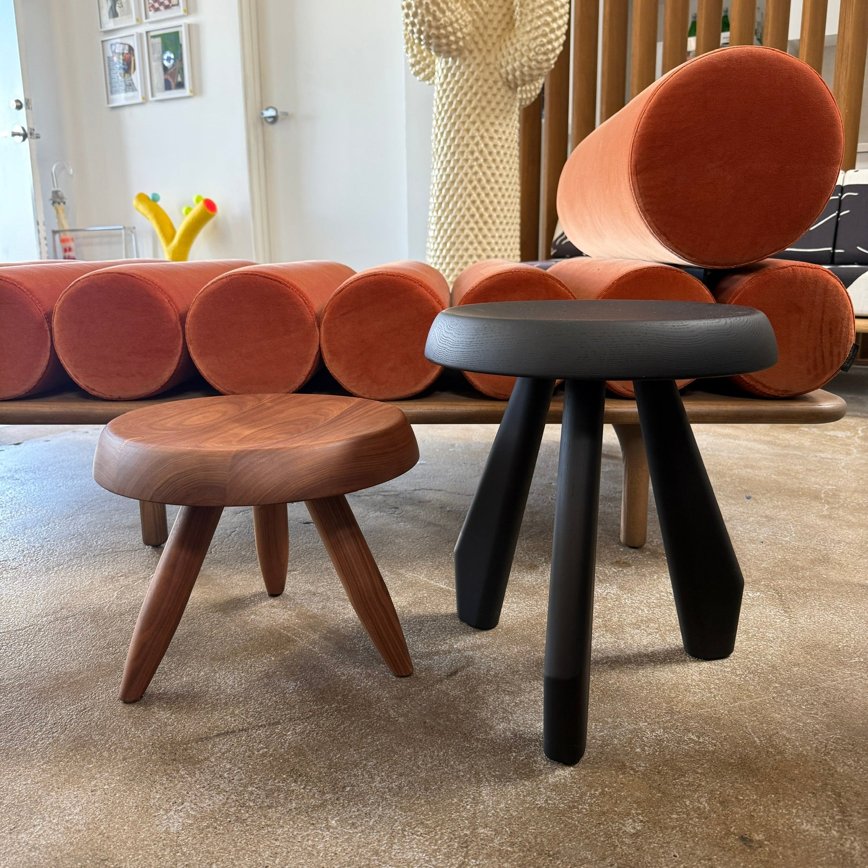 The Cassina 523 Tabouret Meribel by Cassina is a small, round, three-legged solid wood stool with a gray seat and black legs, shown against a plain white background.