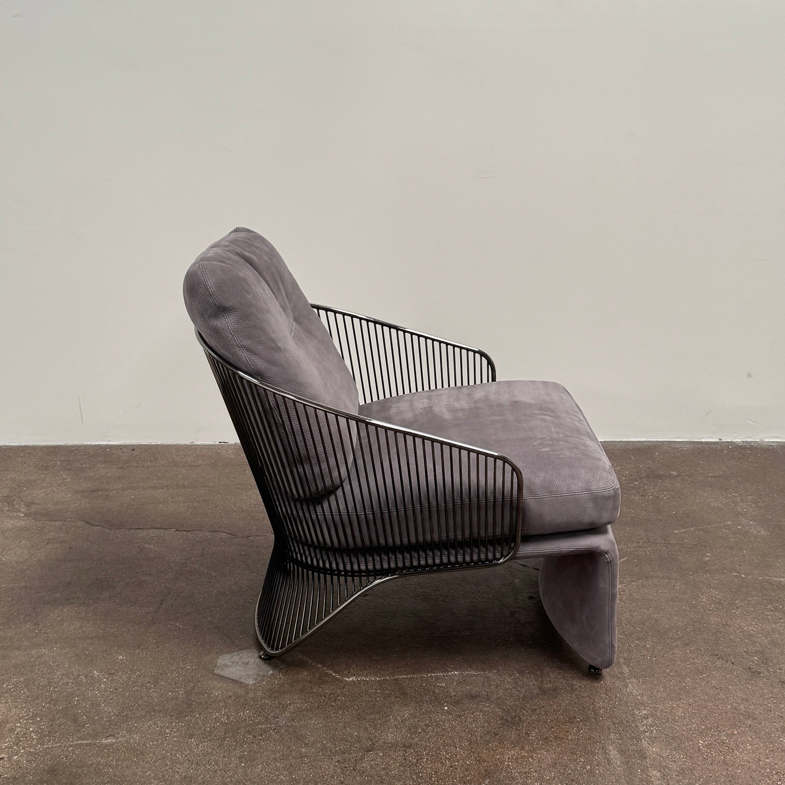 A set of two Minotti Colette Lounge Chairs by Minotti is displayed side by side against a plain white background. Each chair showcases luxurious gray nubuck leather upholstery and sleek black metal armrests, elegantly capturing the timeless mid-century silhouette characteristic of the iconic design.