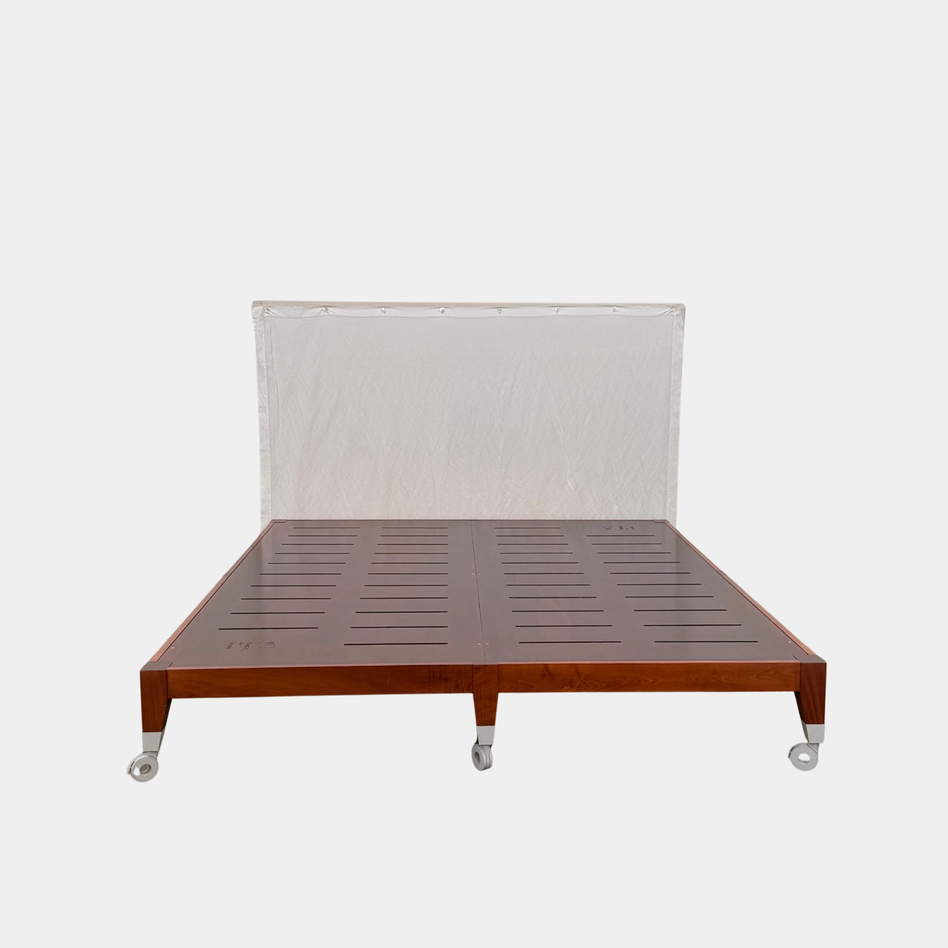 The Driade King Size bed by Modern Resale features a slatted wooden frame on wheels, set against a plain white wall and headboard on a concrete floor.