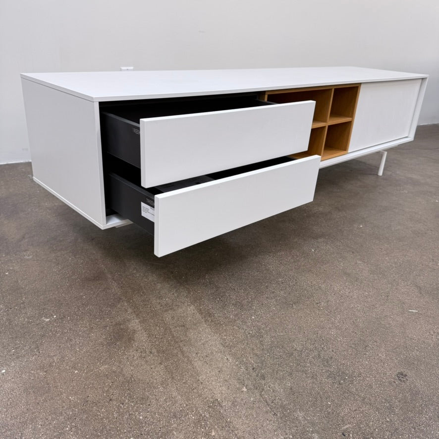 Low-profile white DWR Treku Aura Media Unit on thin legs, featuring two side cabinets and a central open shelf section with a wood-toned interior.