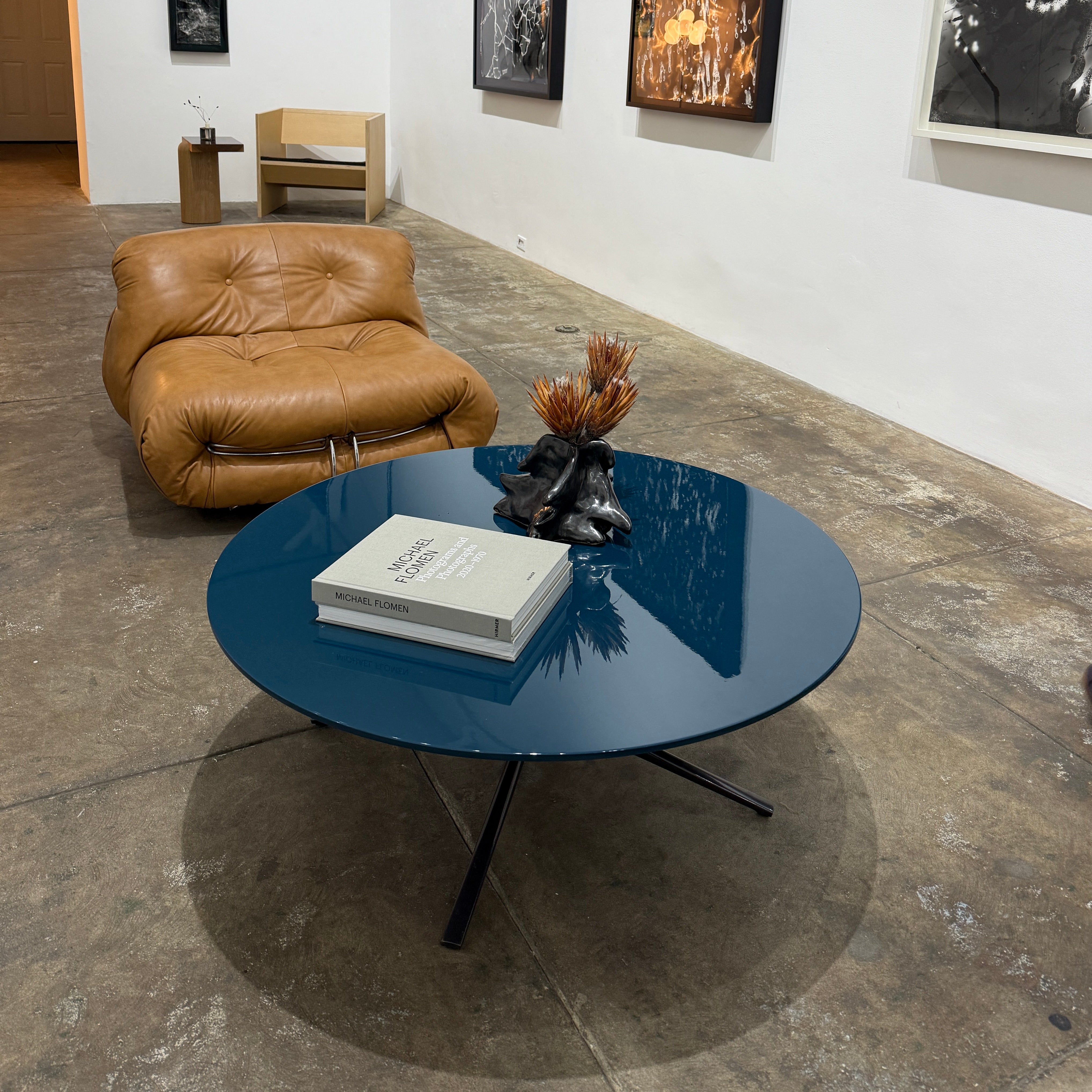 The Poliform Mondrian Lacquered Coffee Table showcases a round blue top with a black, four-legged metal base against a white background.
